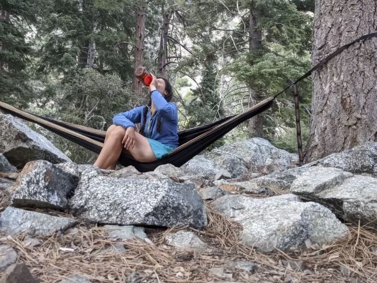 woman drinking from a nalgene water bottle in a hammock in the forest