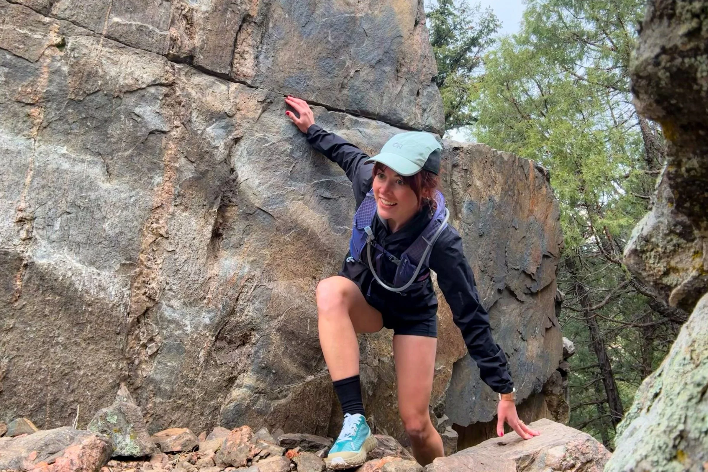 Woman scrambling across mountain rocks while wearing Nathan VaporAir gear.