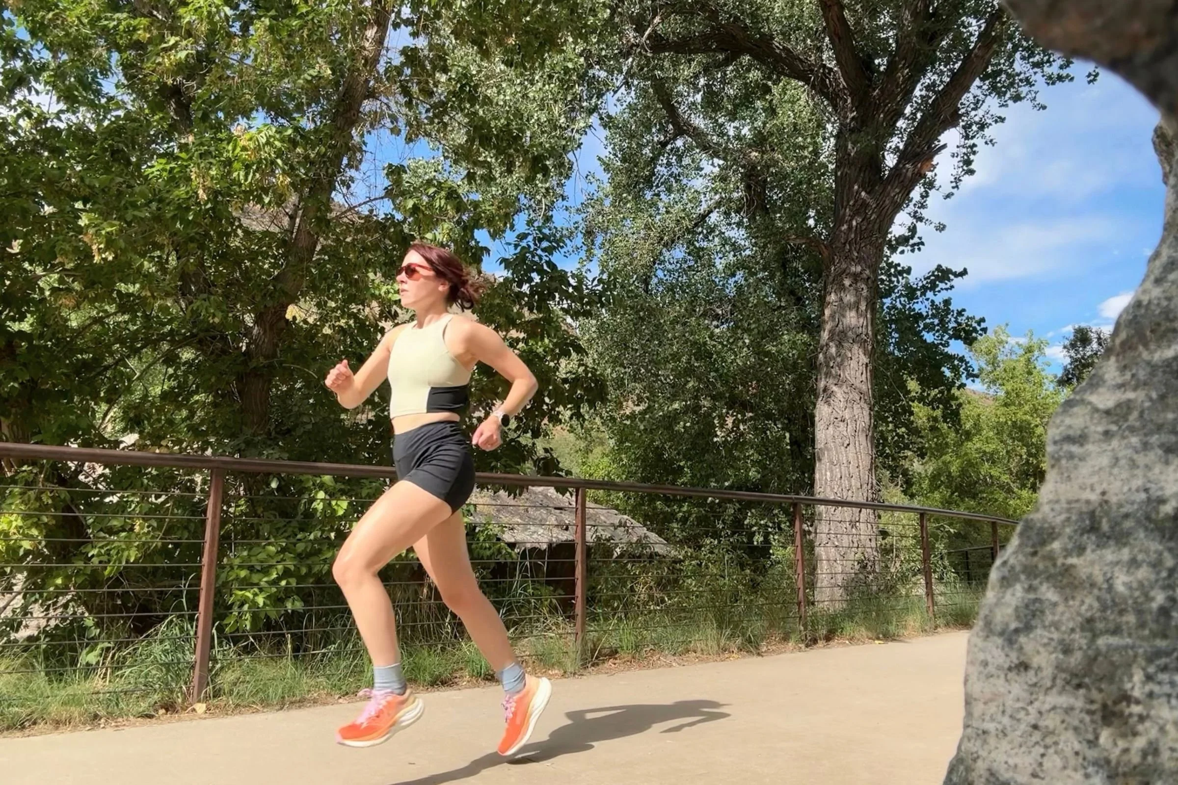 A woman wearing Saucony Ride 19 Road Running Shoes runs along a pathway with trees in the background.