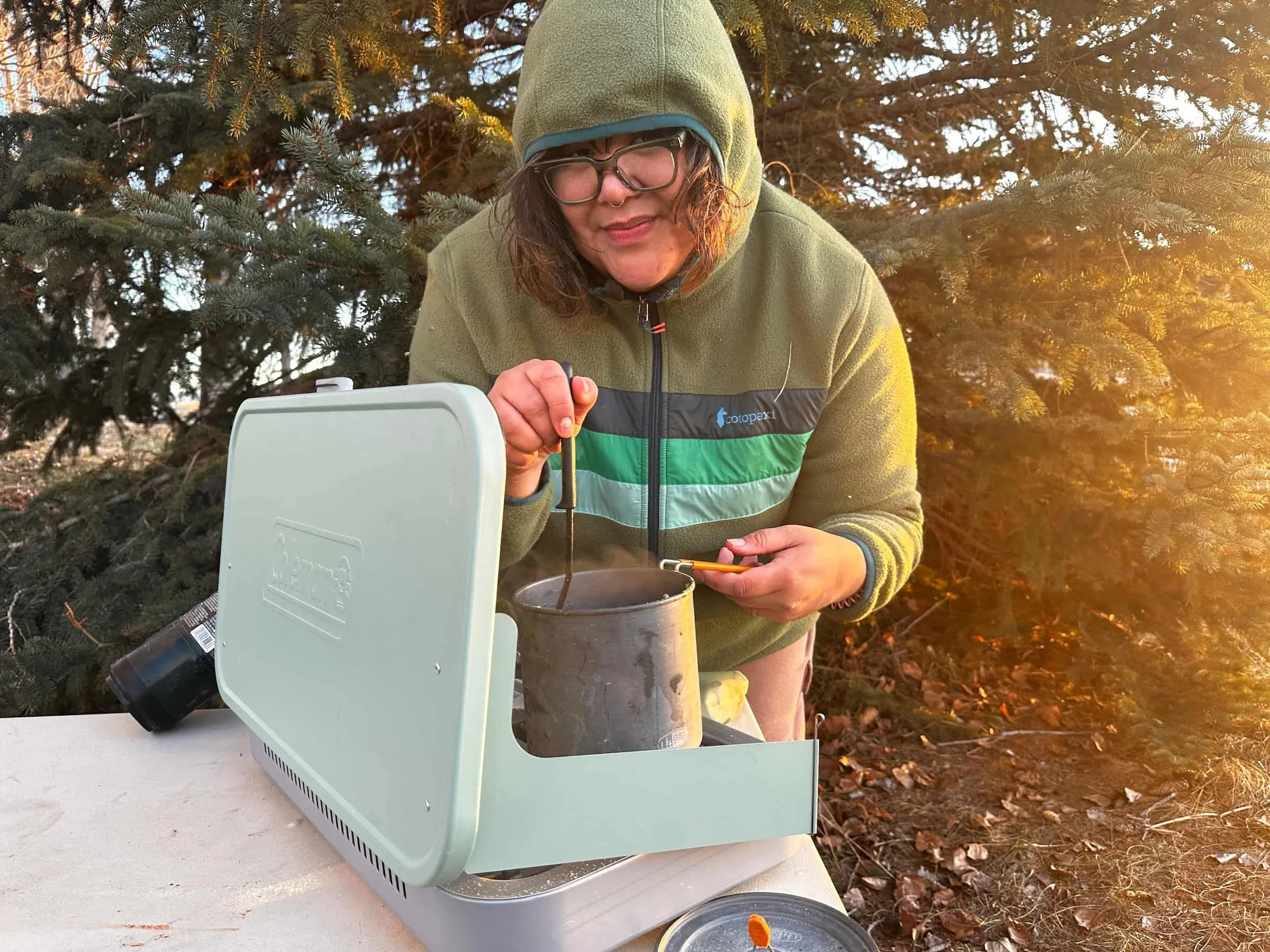 camper with glasses cooking in a campsite on a campstove