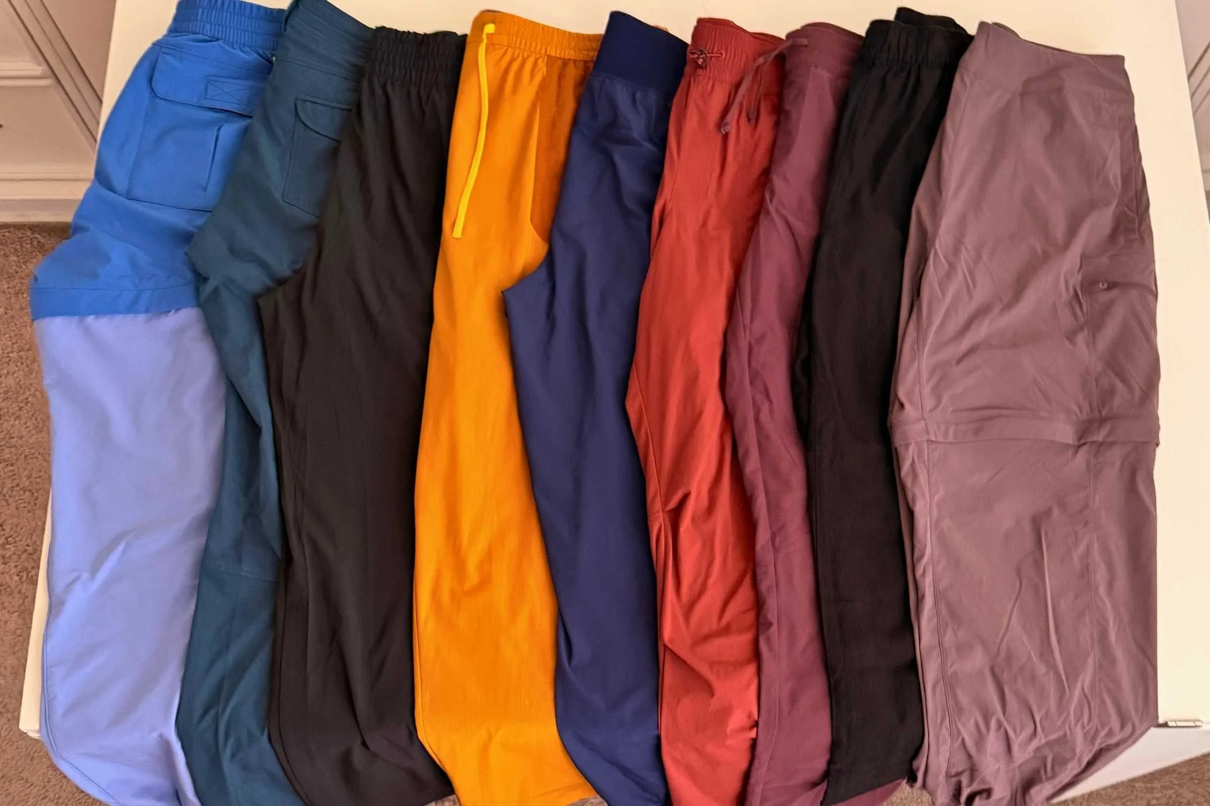Nine pairs of travel pants side-by-side laid flat
