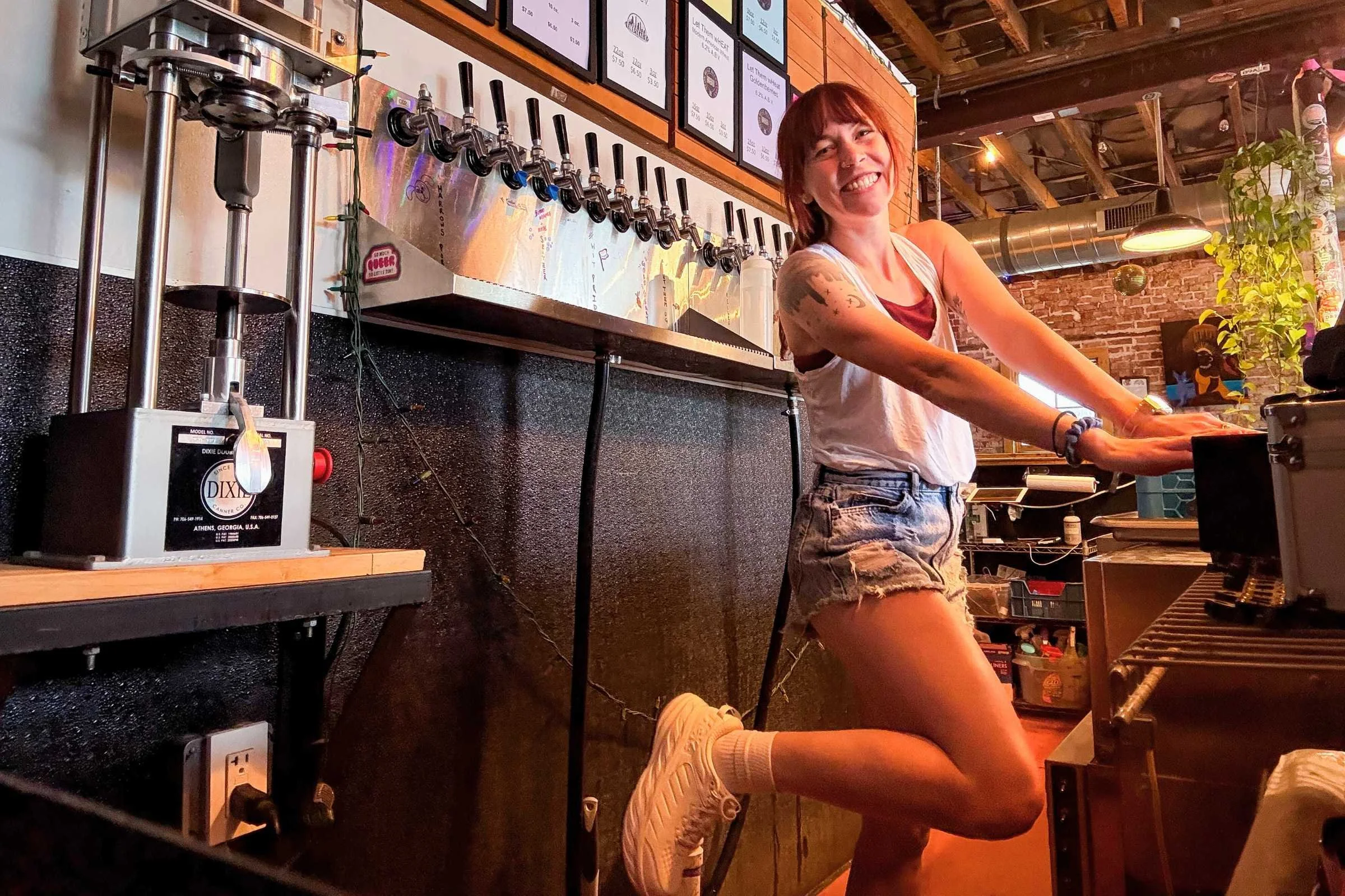smiling woman behind the bar at a brewery wearing white hoka bondi sr shoes