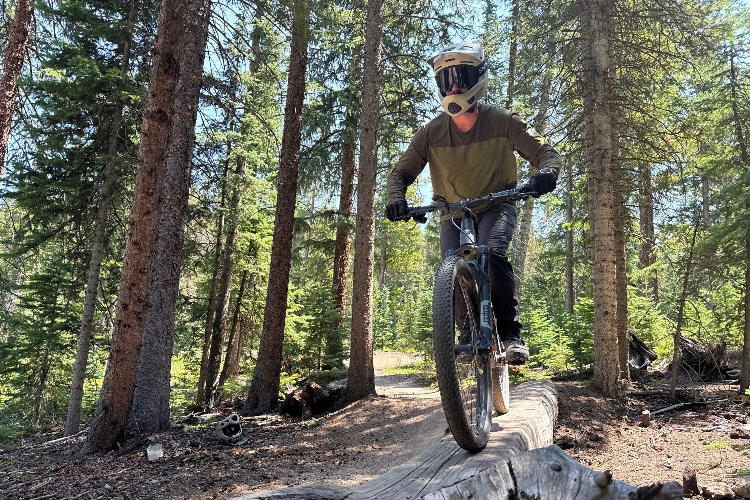 A man wearing a Smith Hardline helmet while riding a mountain bike across a fallen log.