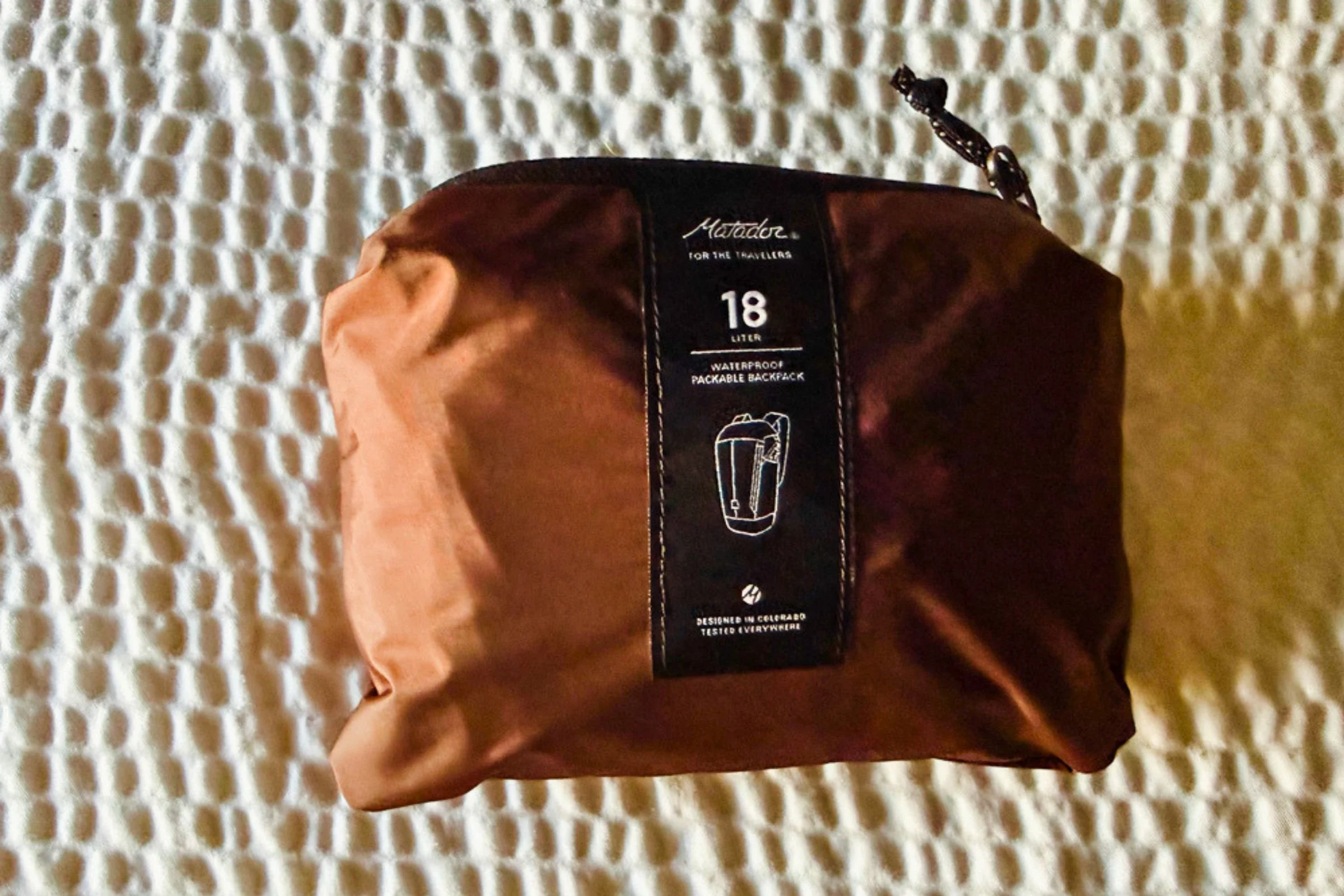 Matador 18L Waterproof Packable Backpack packed into its zippered pouch on a textured white surface.
