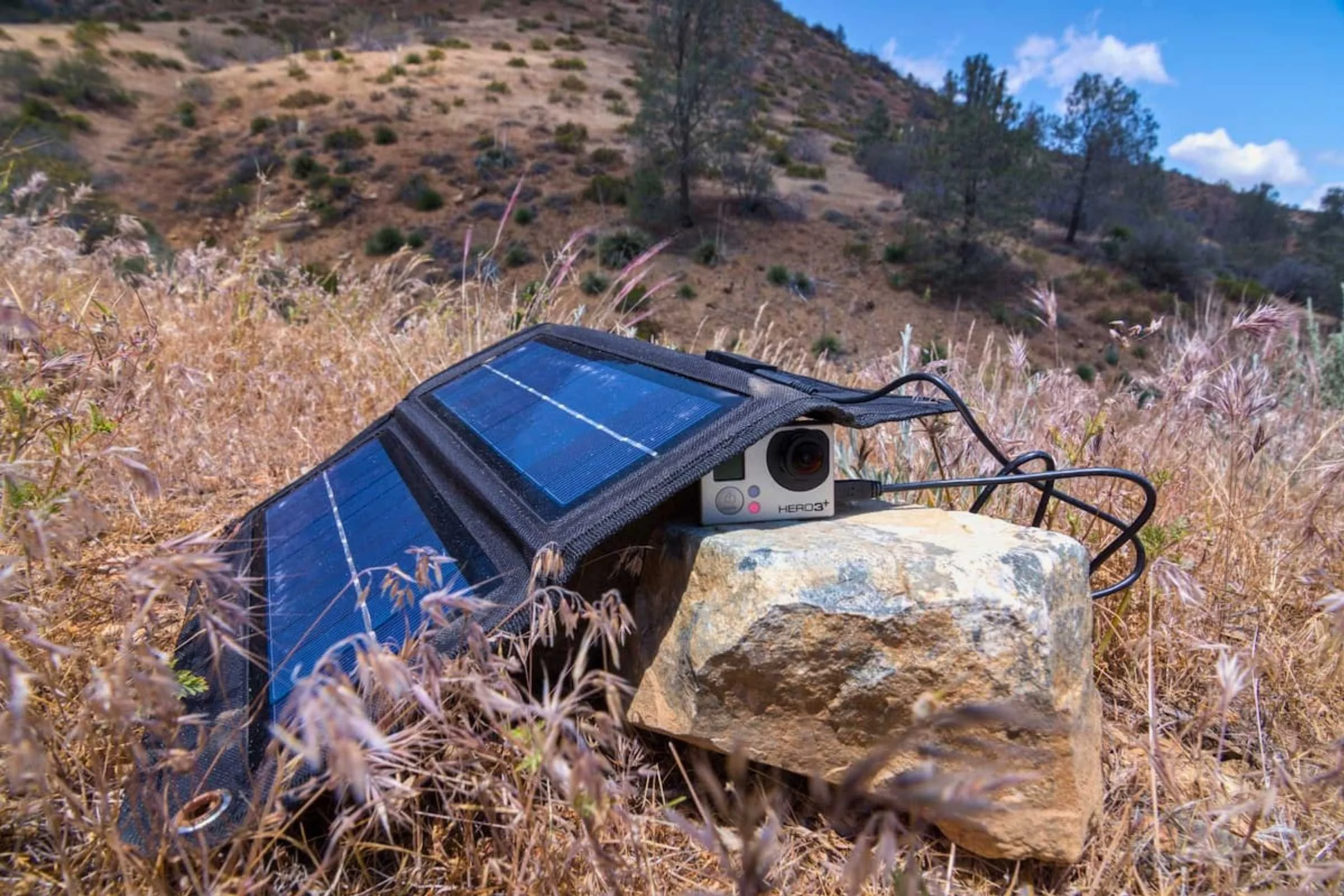 A solar panel charging a GoPro Hero camera in a field