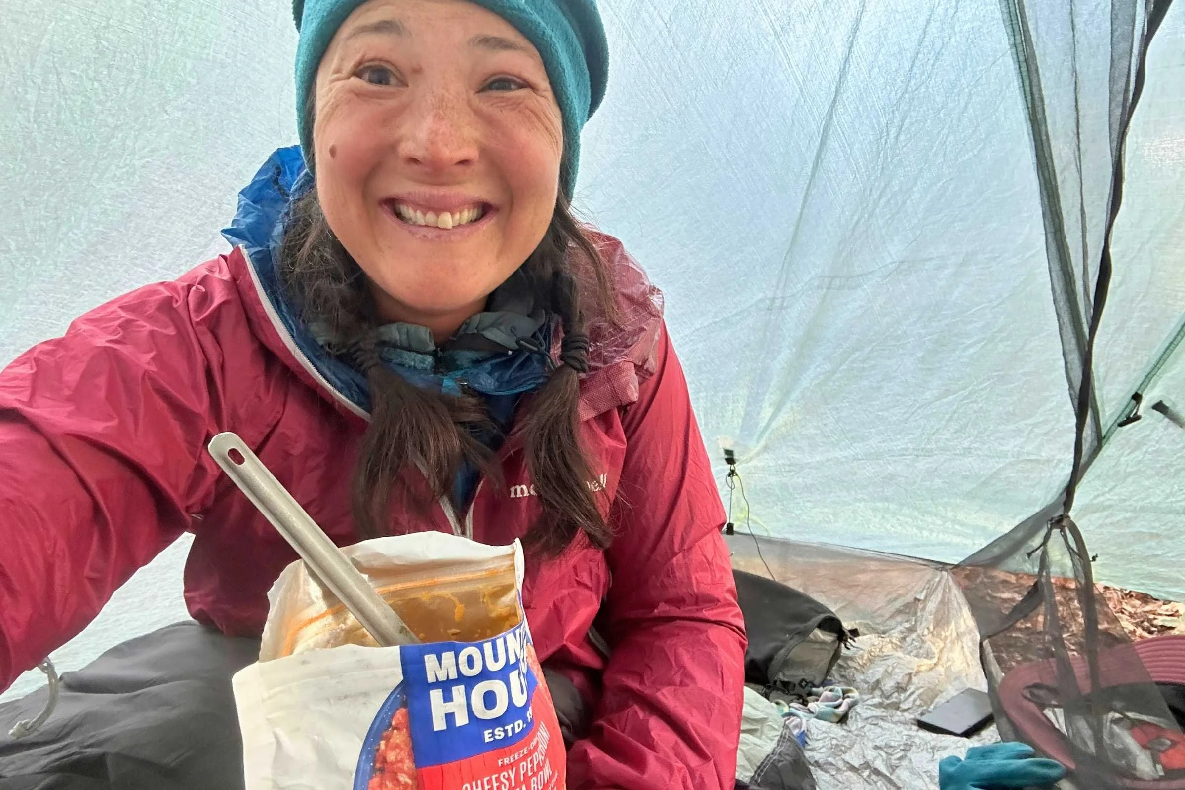 Woman inside a tent eating Mountain House Cheesy Pepperoni Pizza Bowl freeze-dried meal.