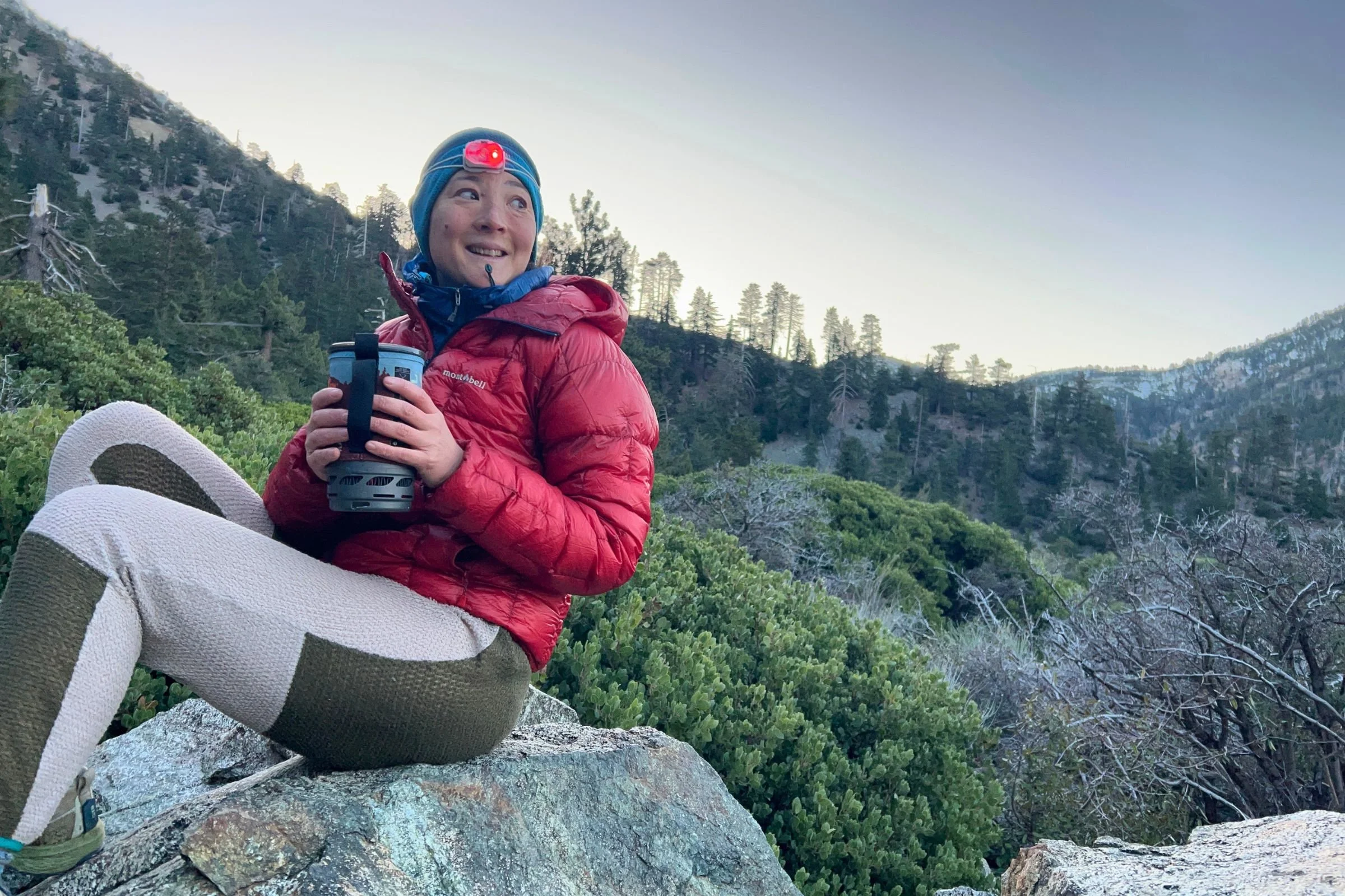 The author wearing the Petzl Swift LT headlamp, while holding a large container of hot coffee. Trees and rock are in the background.