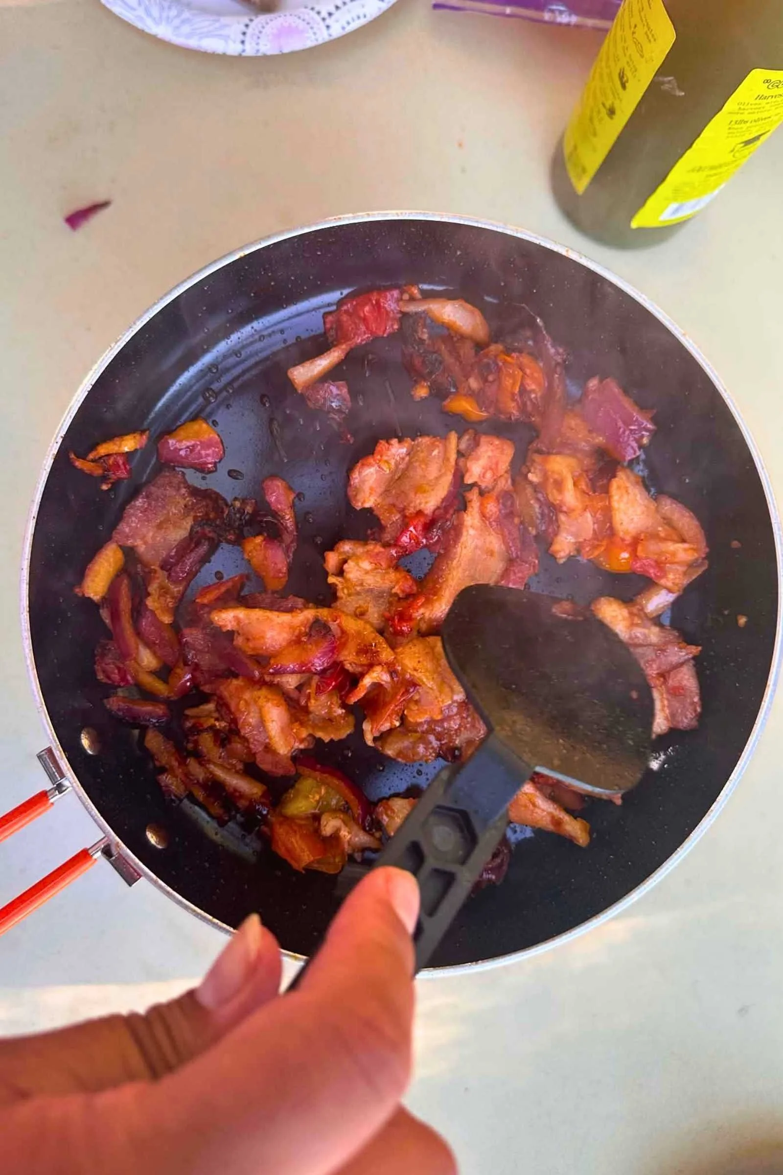 Bacon cooking in the Jetboil TrailCook with a hand holding a spatula.