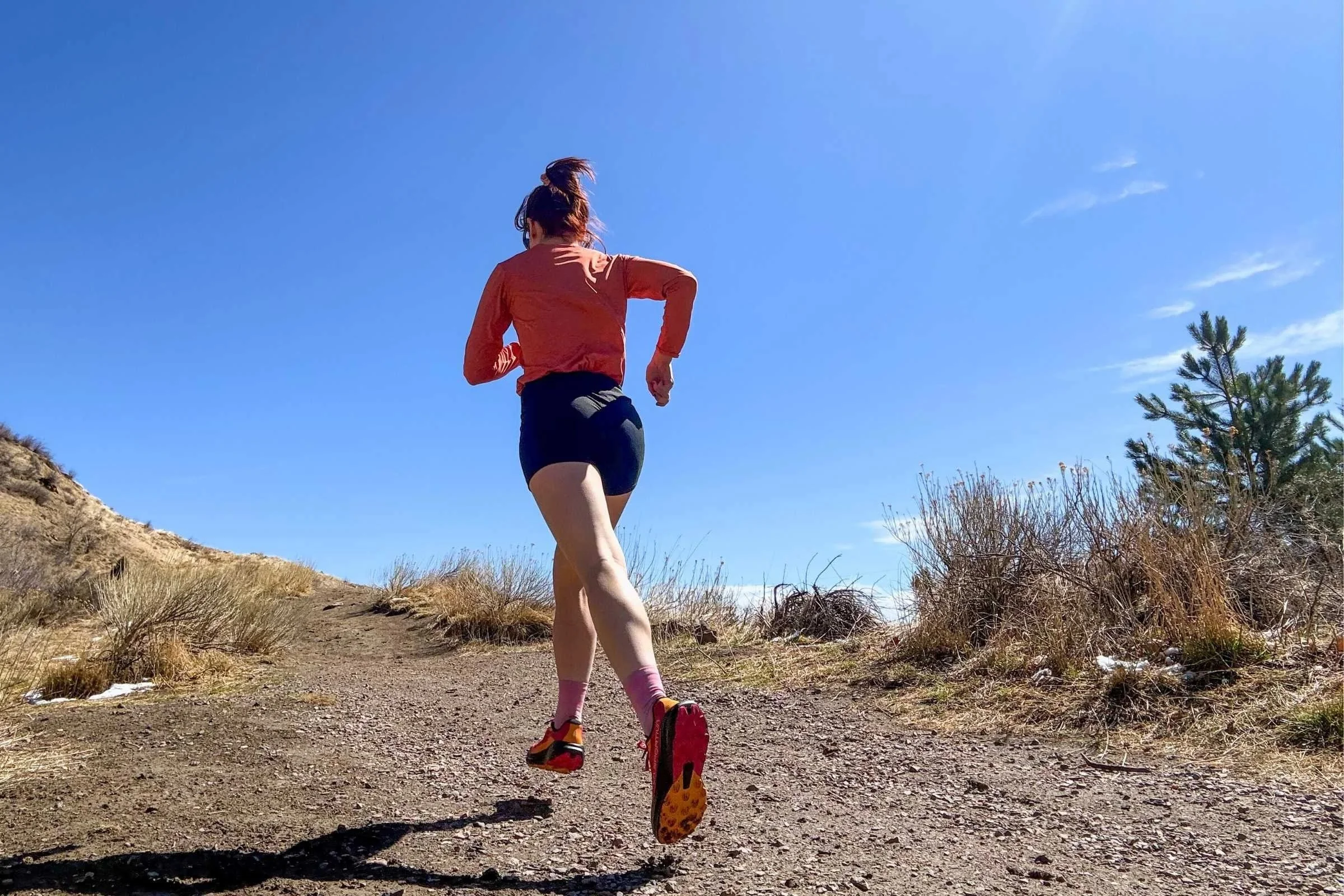 Woman wearing the La Sportiva Prodigio 2 trail running shoes on a gravel trail with brush and trees in the background.