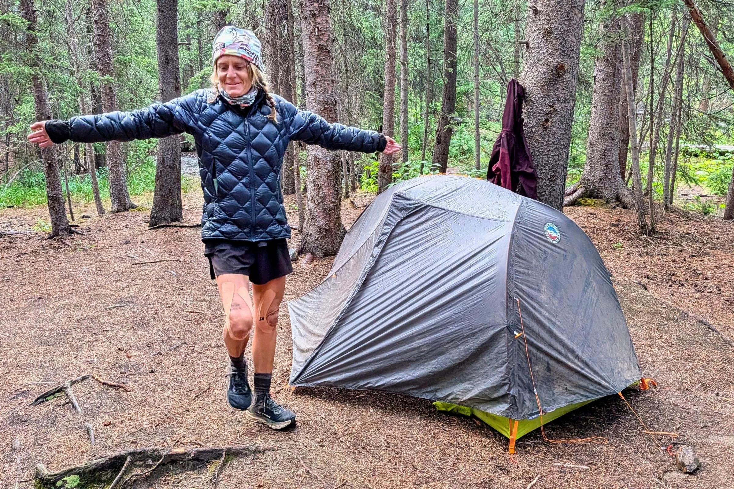 A person standing outside of the Big Agnes Tiger Wall UL1 Bikepack Tent with trees in the background.