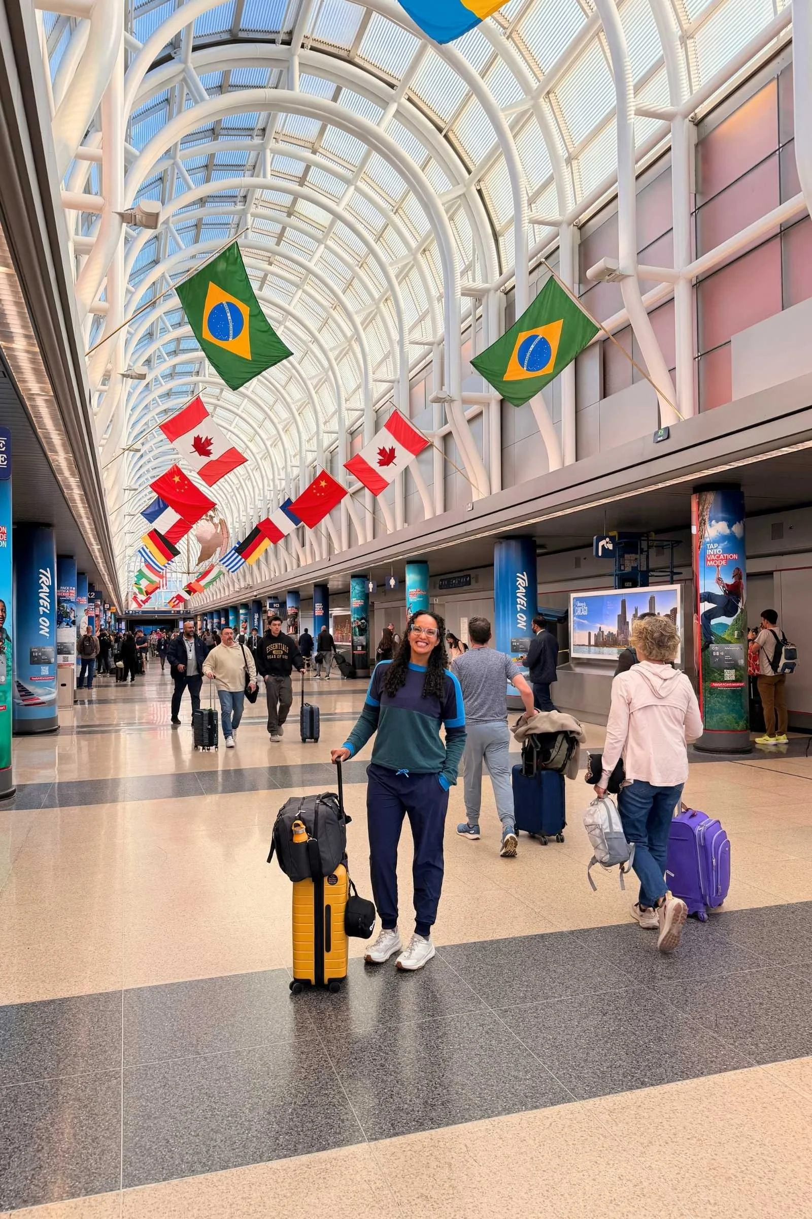 Woman wearing Cotopaxi Cambio Jogger travel pants in navy blue in an airport with various country flags mounted near the ceiling