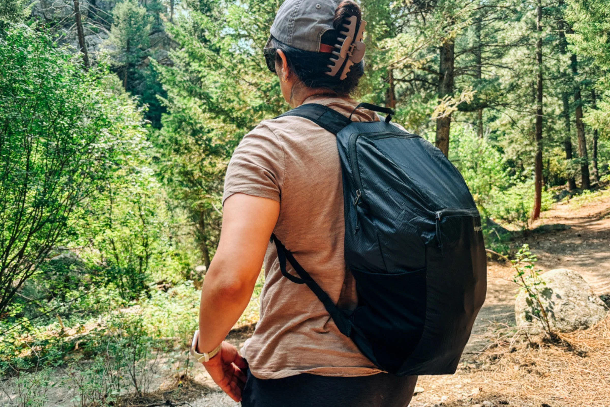 Woman wearing a black Eagle Creek Packable Backpack while walking along a trail, with the backpack’s pockets visible.