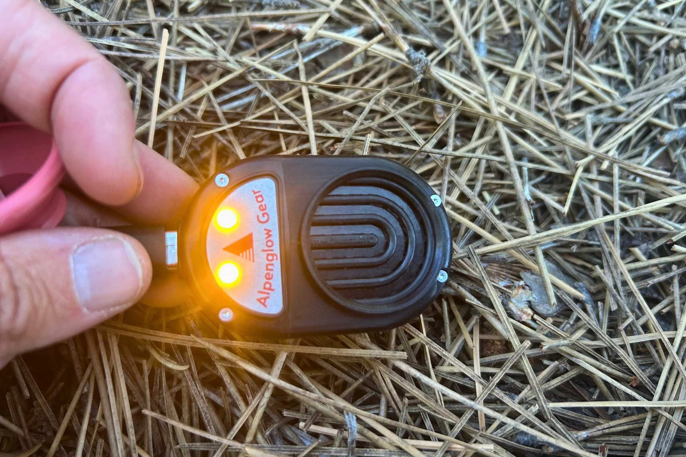 Alpenblow Lux flashlight held in a grassy outdoor setting by a person.