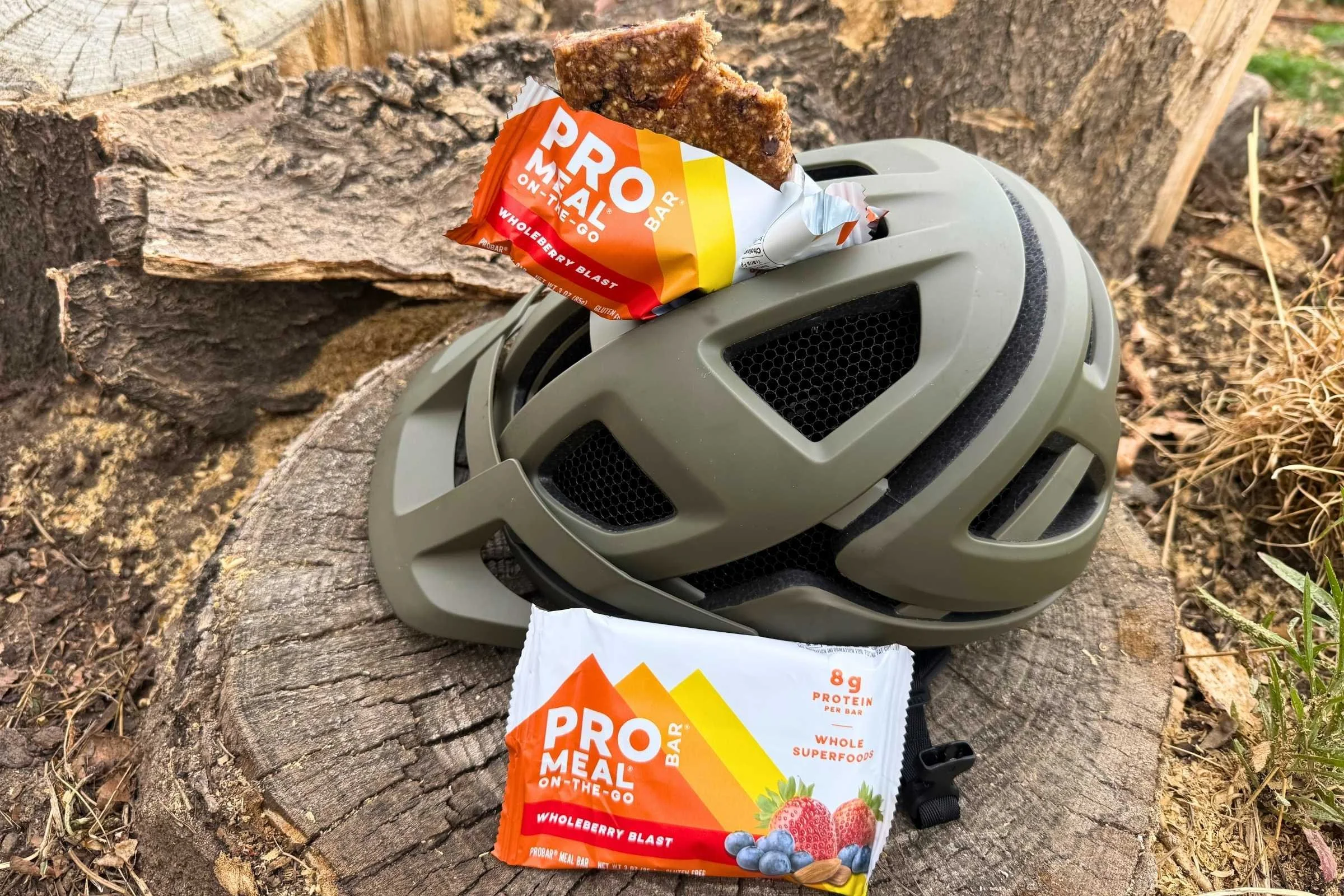 a mountain bike helmet on a log with one probar meal bar resting beside the helmet and another sticking out of the helmet