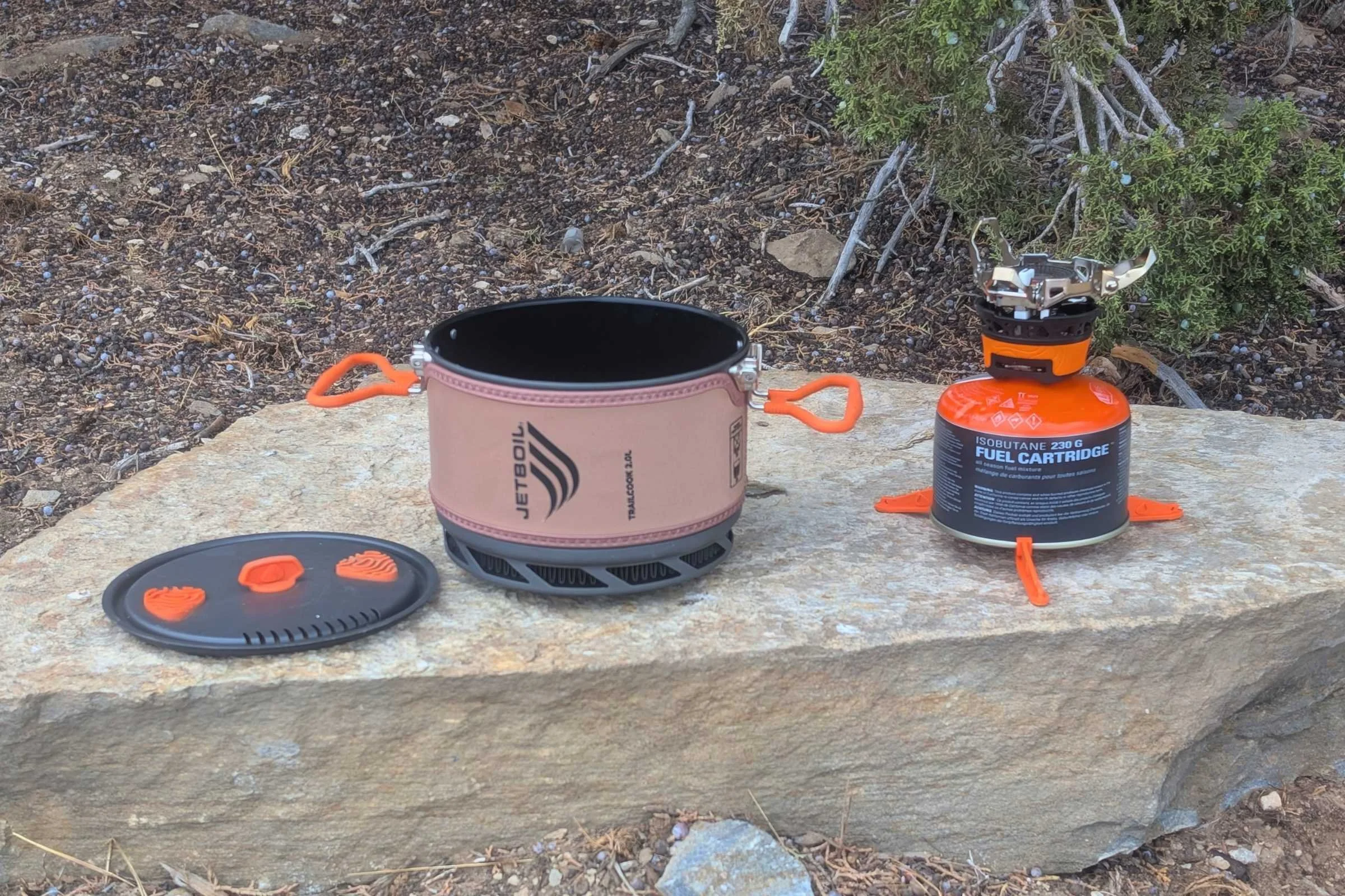 Closeup of the Jetboil TrailCook lid, pot, and burner in a row on a rock.