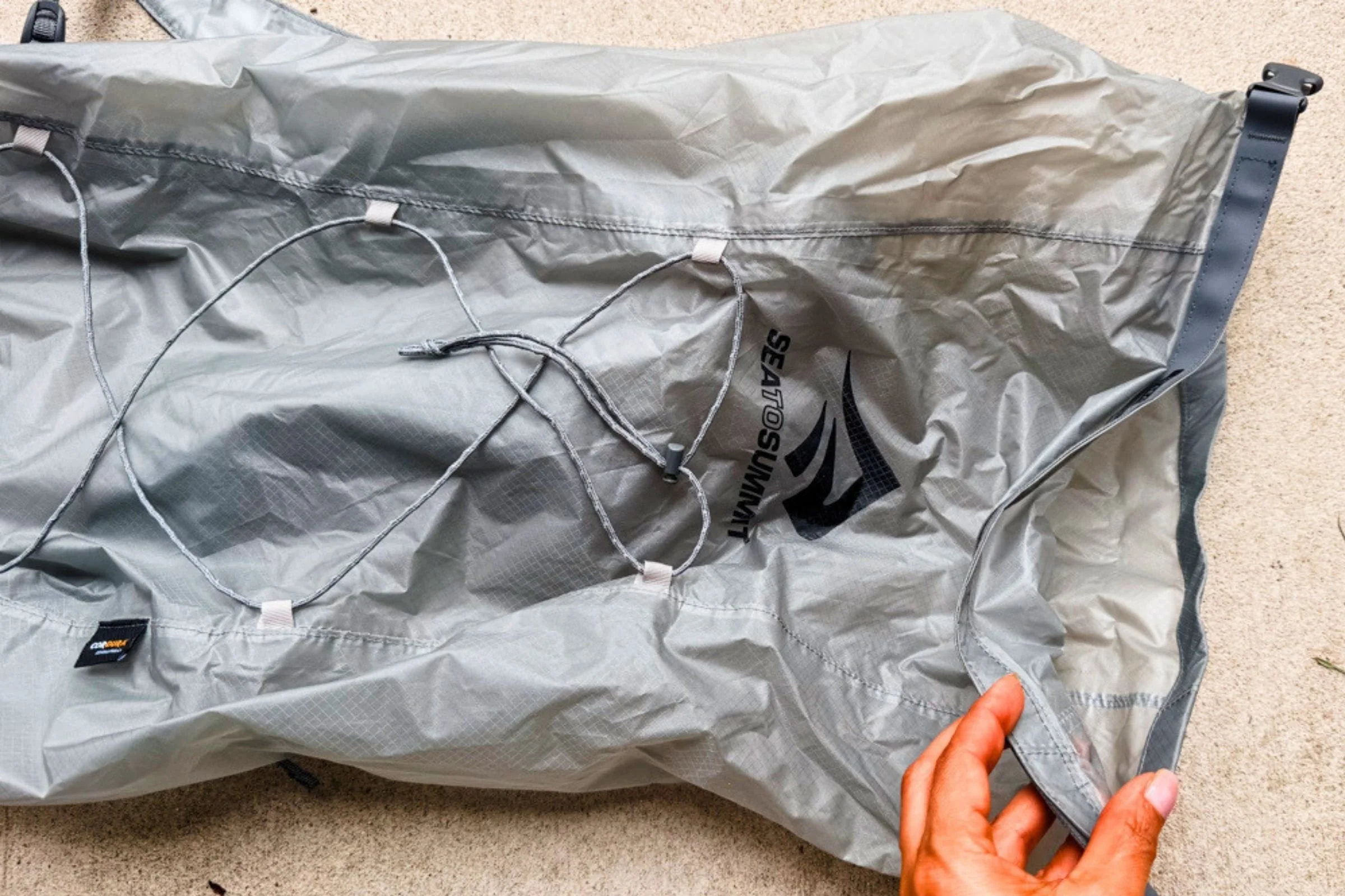 A hand opens the roll-top closure of the Sea to Summit Ultra-Sil Dry Daypack, with front bungee cords visible