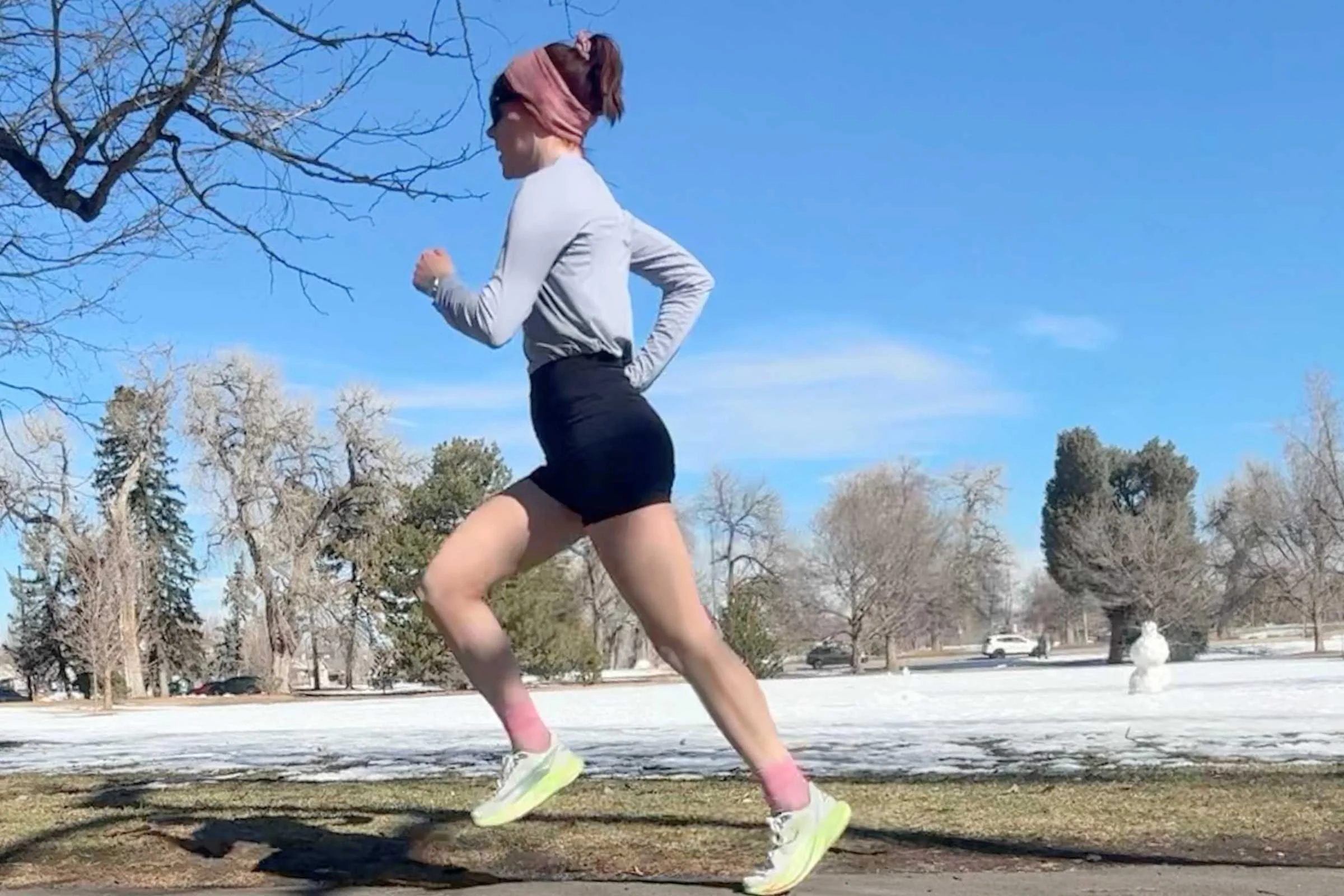 Woman running on a snowy park path wearing REI Co-op Swiftland Grid Running Shirt.