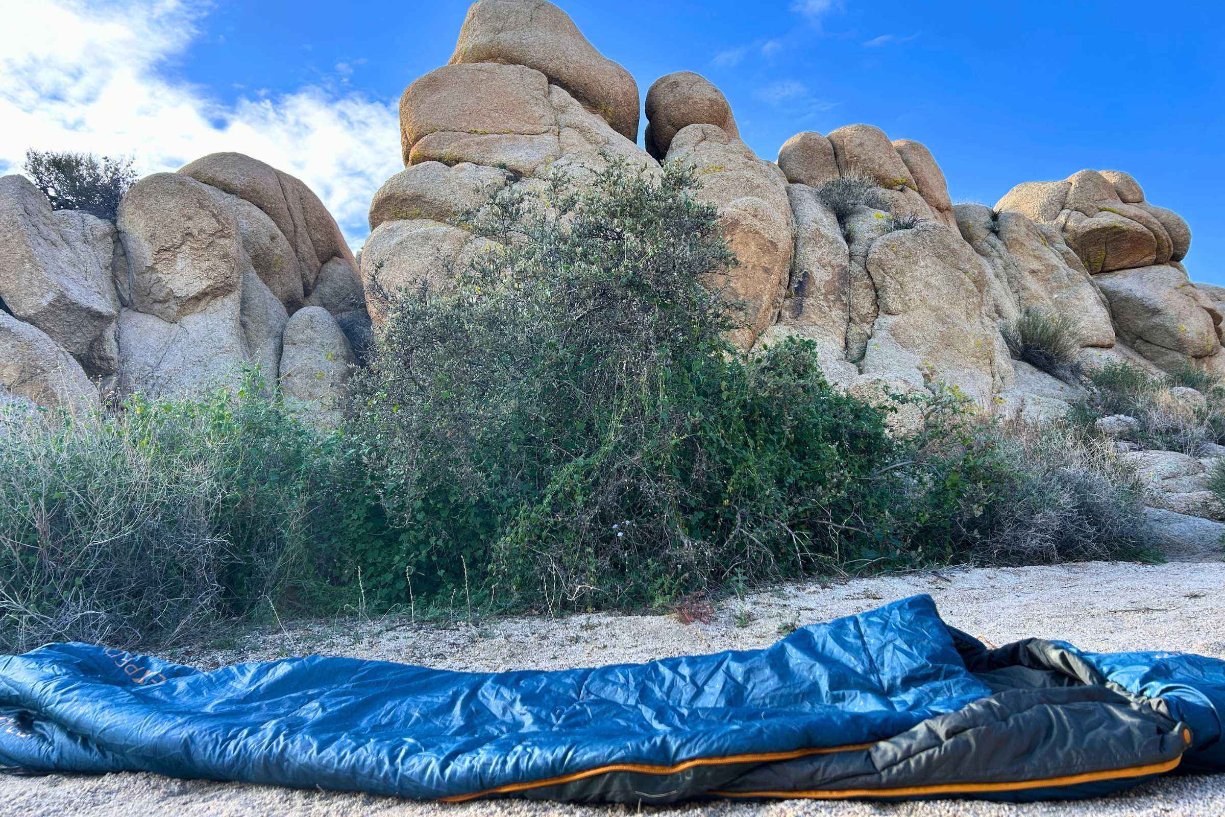 blue exped deepsleep sleeping bag laid out on the ground with rock structures in the background