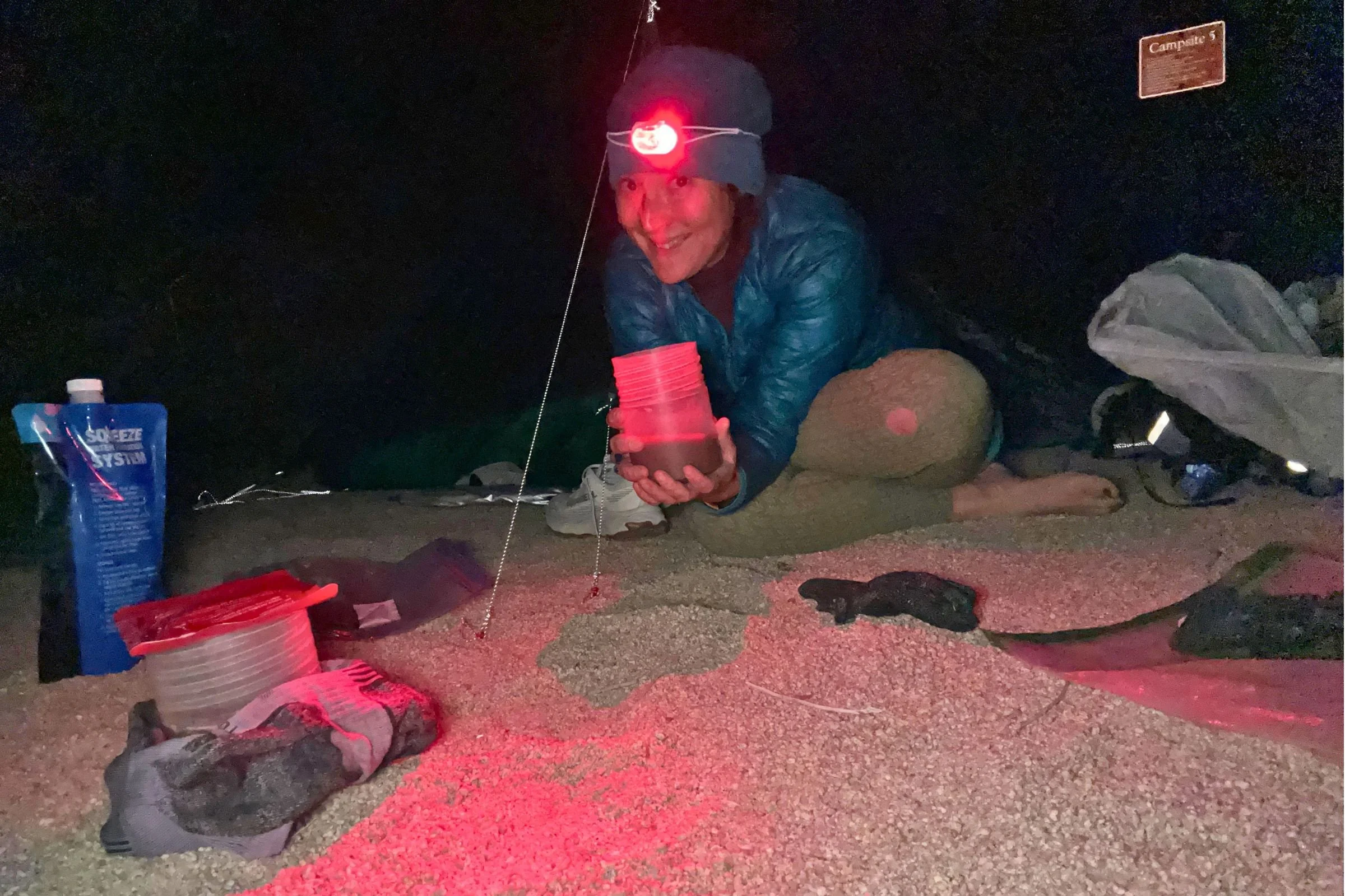 The author wearing the Petzl Swift LT headlamp in red light mode, with assorted backpacking gear in the background.