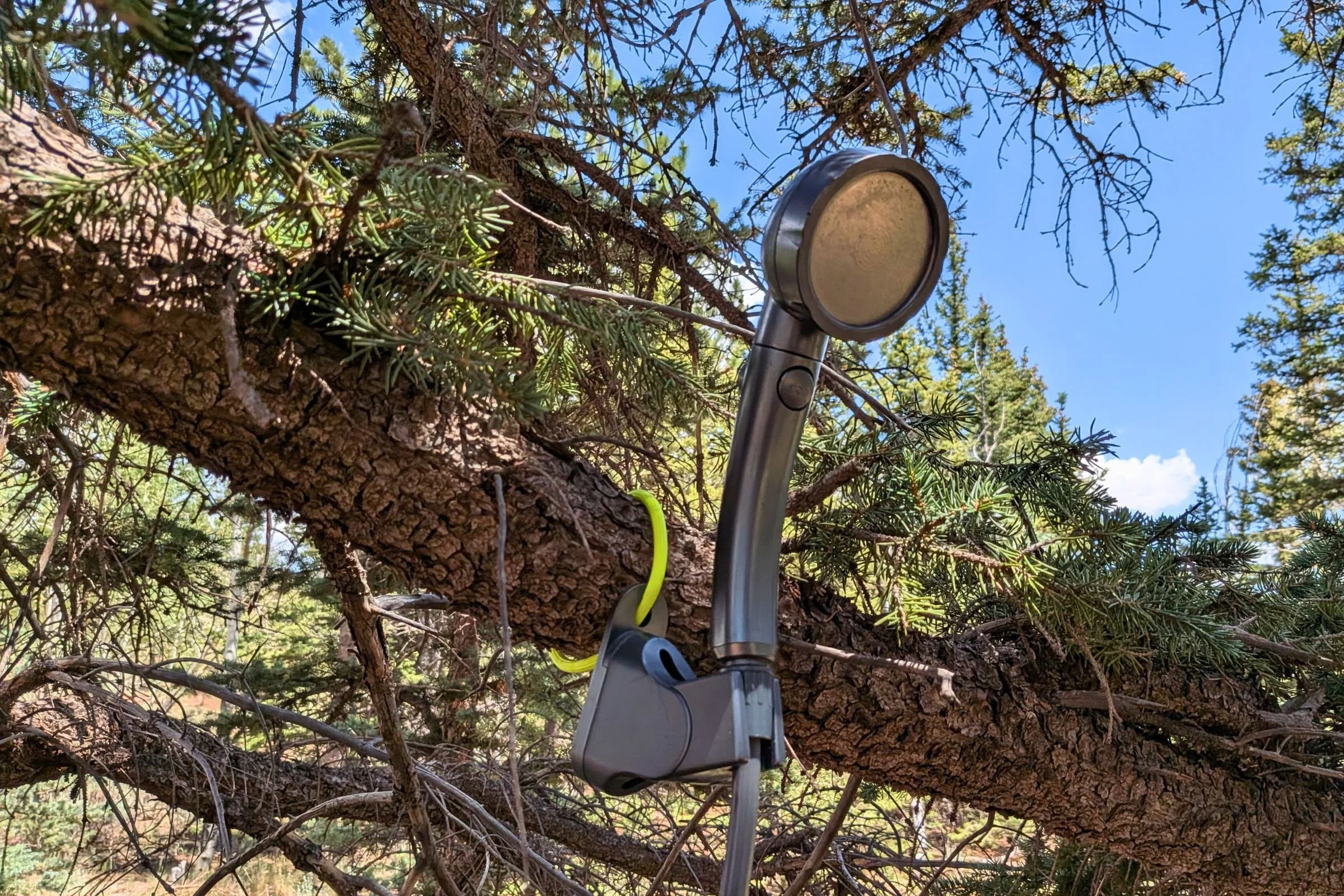 The BougeRV Portable Propane Outdoor Water Heater's shower wand attached to a tree branch