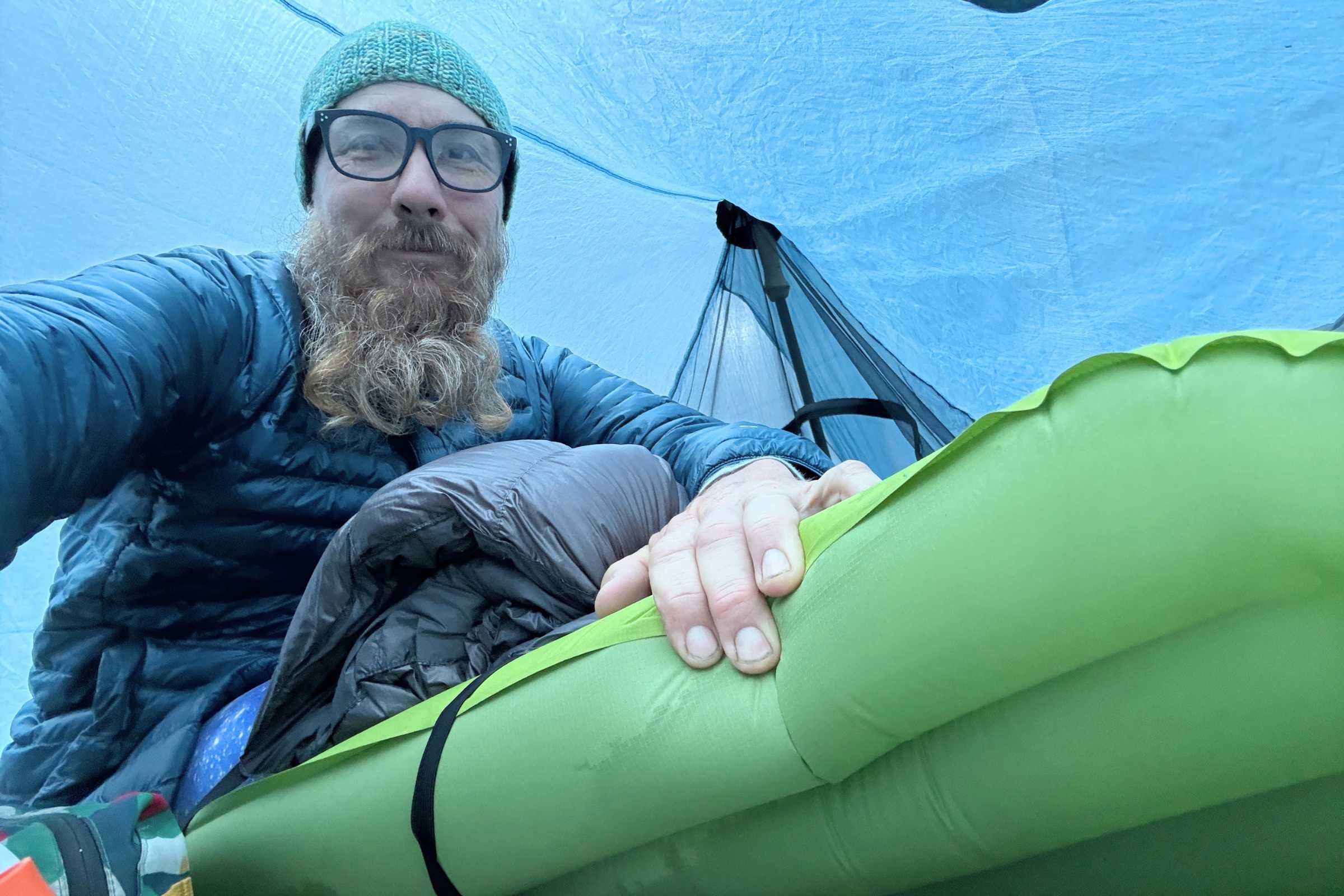 Backpacker inside tent lifting the edge of the EXPED Ultra 6.5R Mummy sleeping pad to show moisture underneath after overnight testing