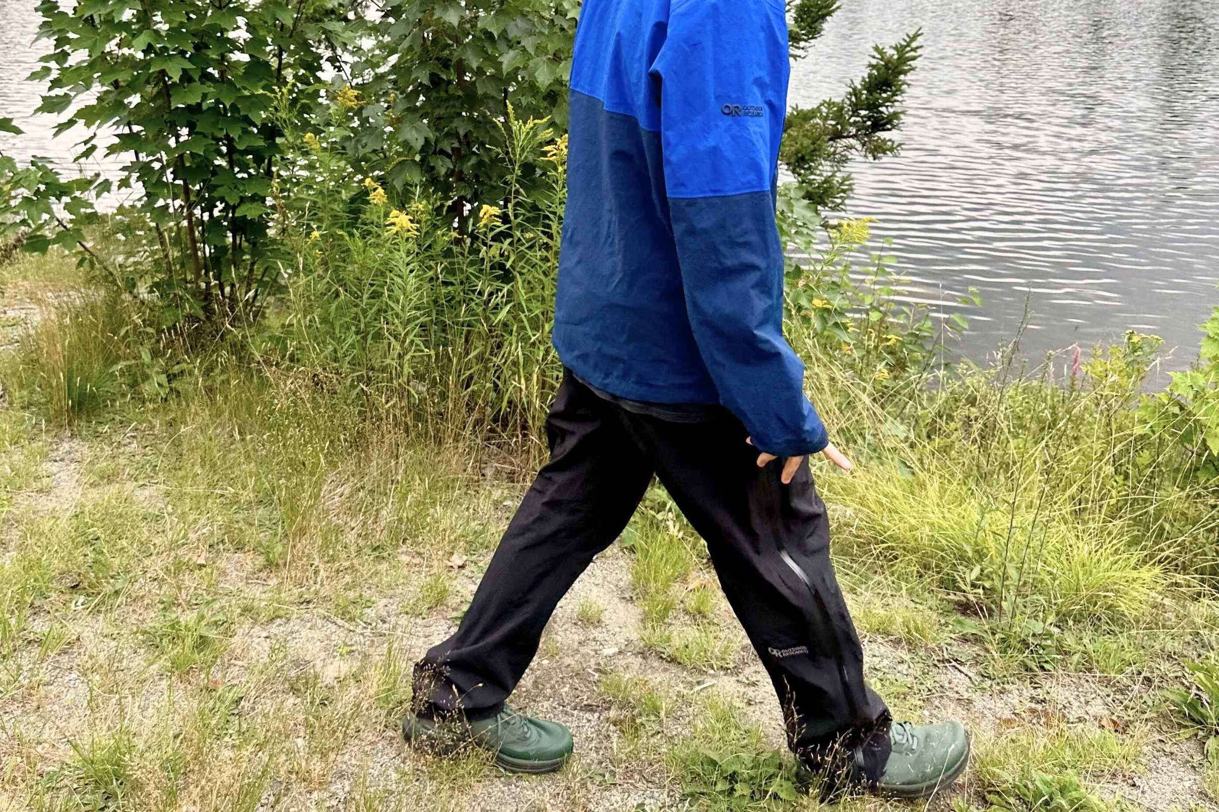 Walking side view of the Outdoor Research Foray rain pants on a lakeside trail.