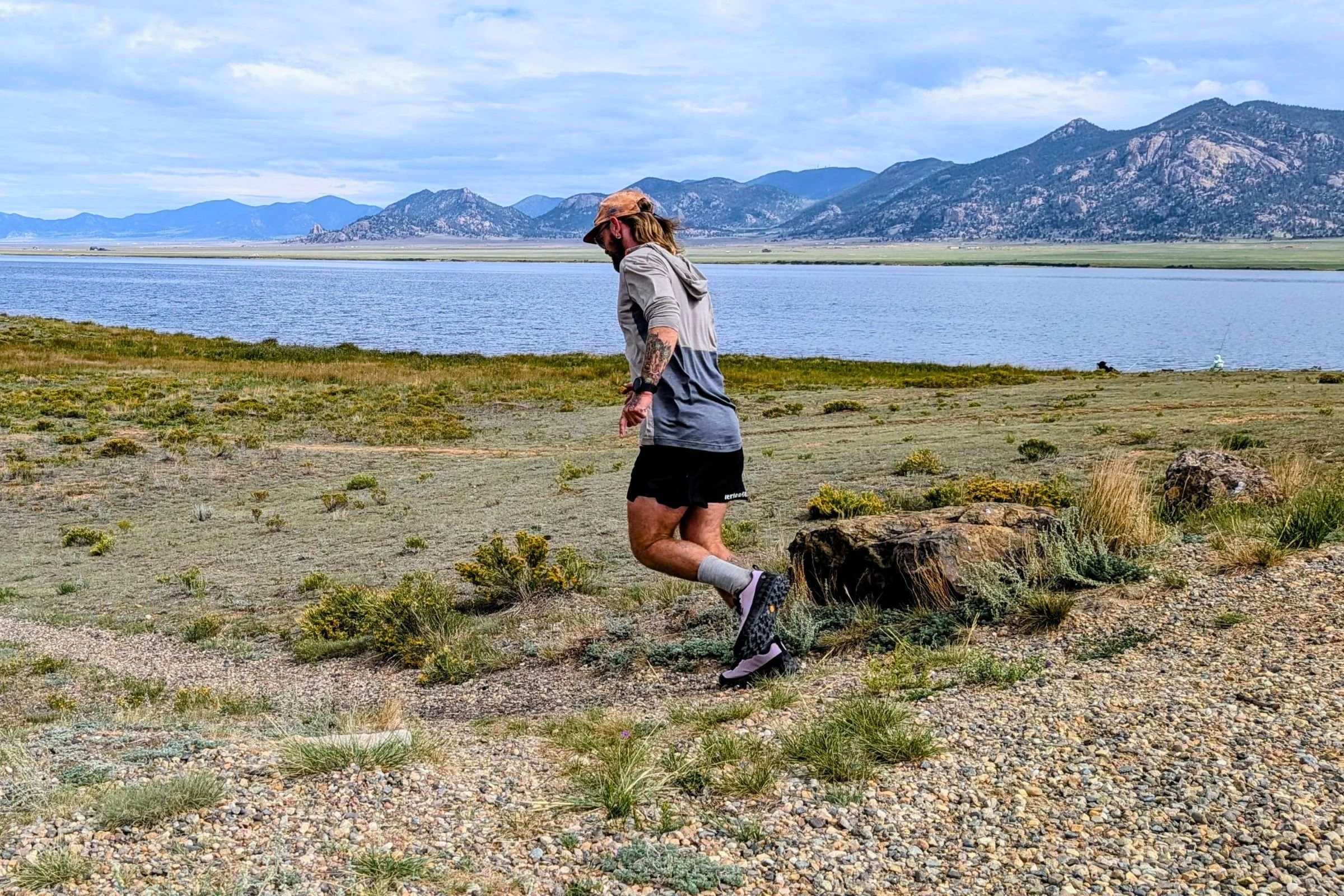 Person running on a trail near a lake while wearing Norda 000 Trail Running Shoes.