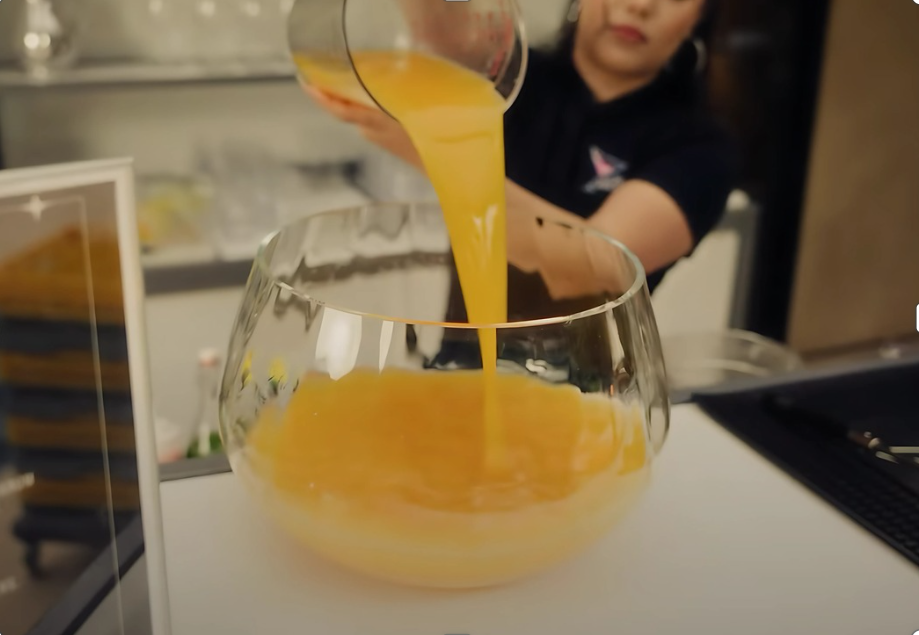 A person pouring orange juice into a large glass bowl.