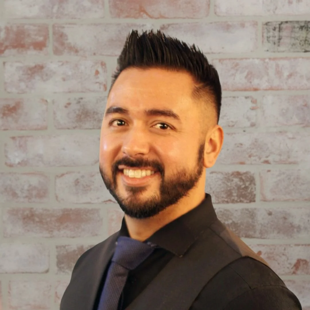 David Eclevia Founder and CEO of Mobile Mixologist in a black suit in front of a white brick wall
