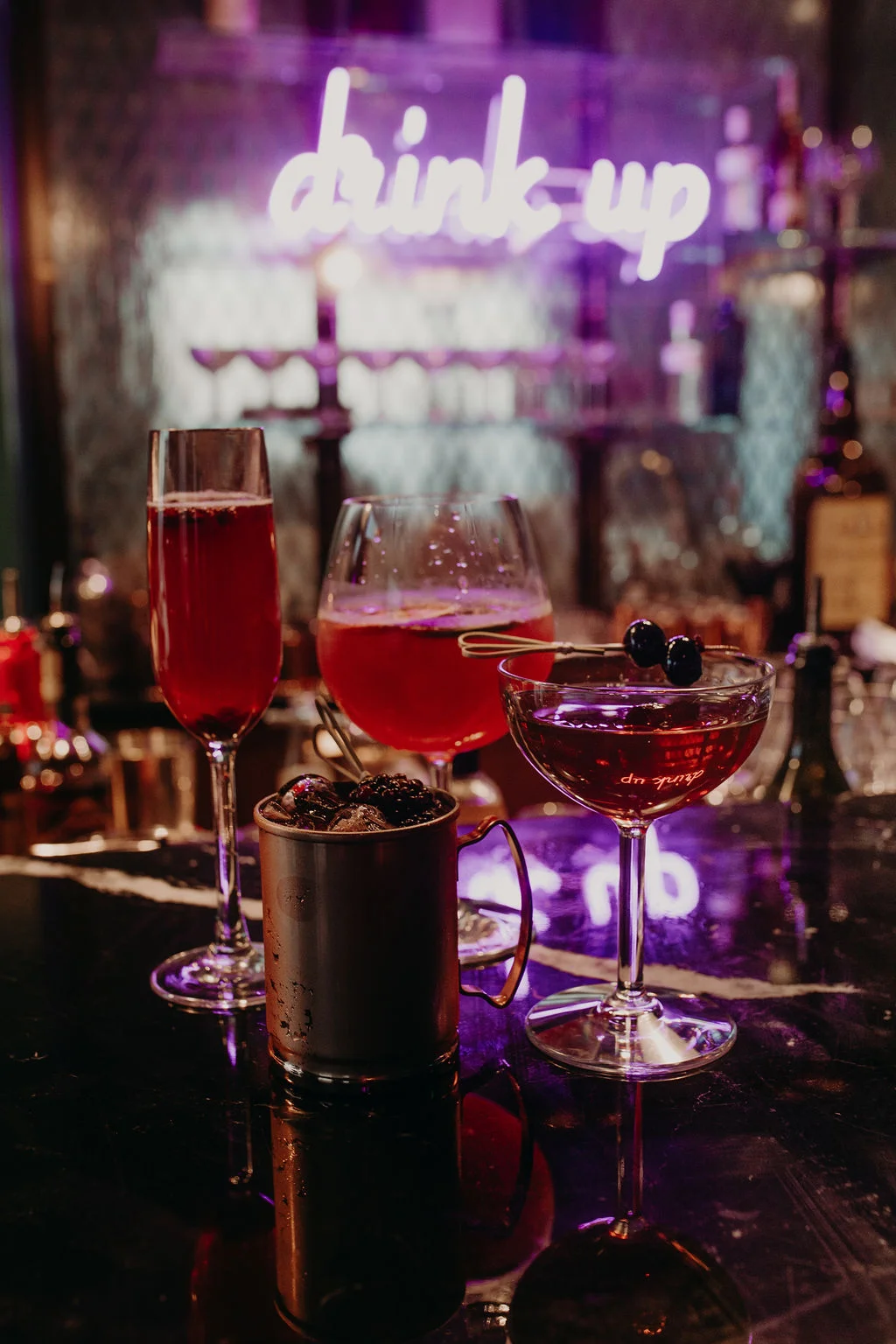 Various colorful cocktails on a black bar counter with a purple neon