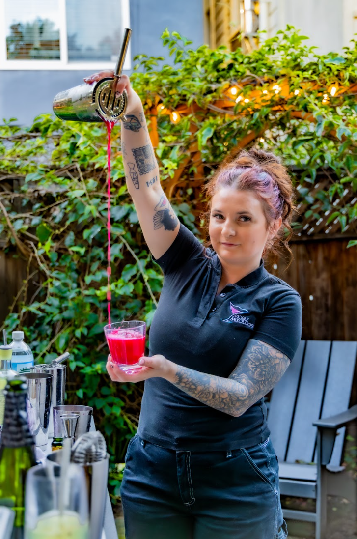 Shawna Pierce Mobile Mixologist Bartender masterfully pouring a red drink into a cup at a garden party in SF