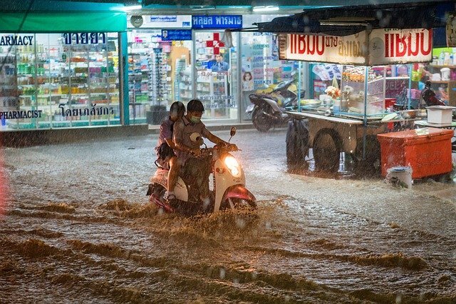 couple riding scooter through a flooded street