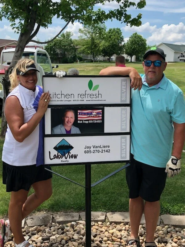 Kitchen Refresh franchisees Jennifer and Chuck Limoges by their hole sponsor sign.