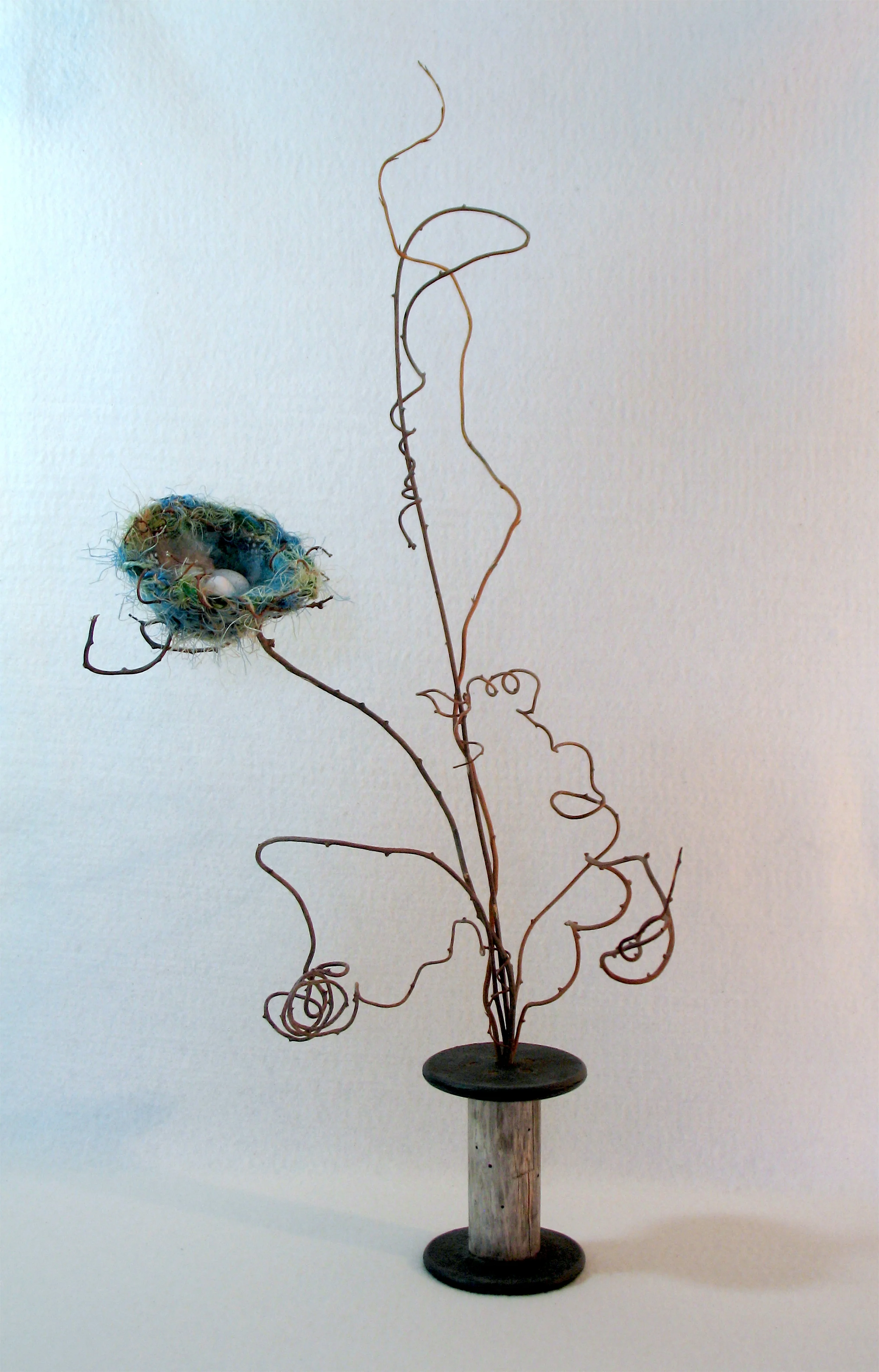 Nest I - Home: Vintage spool, found sticks, willow fronds, fabric strips, yarn, thread, found feathers and (broken) robin's eggs. (25" tall)