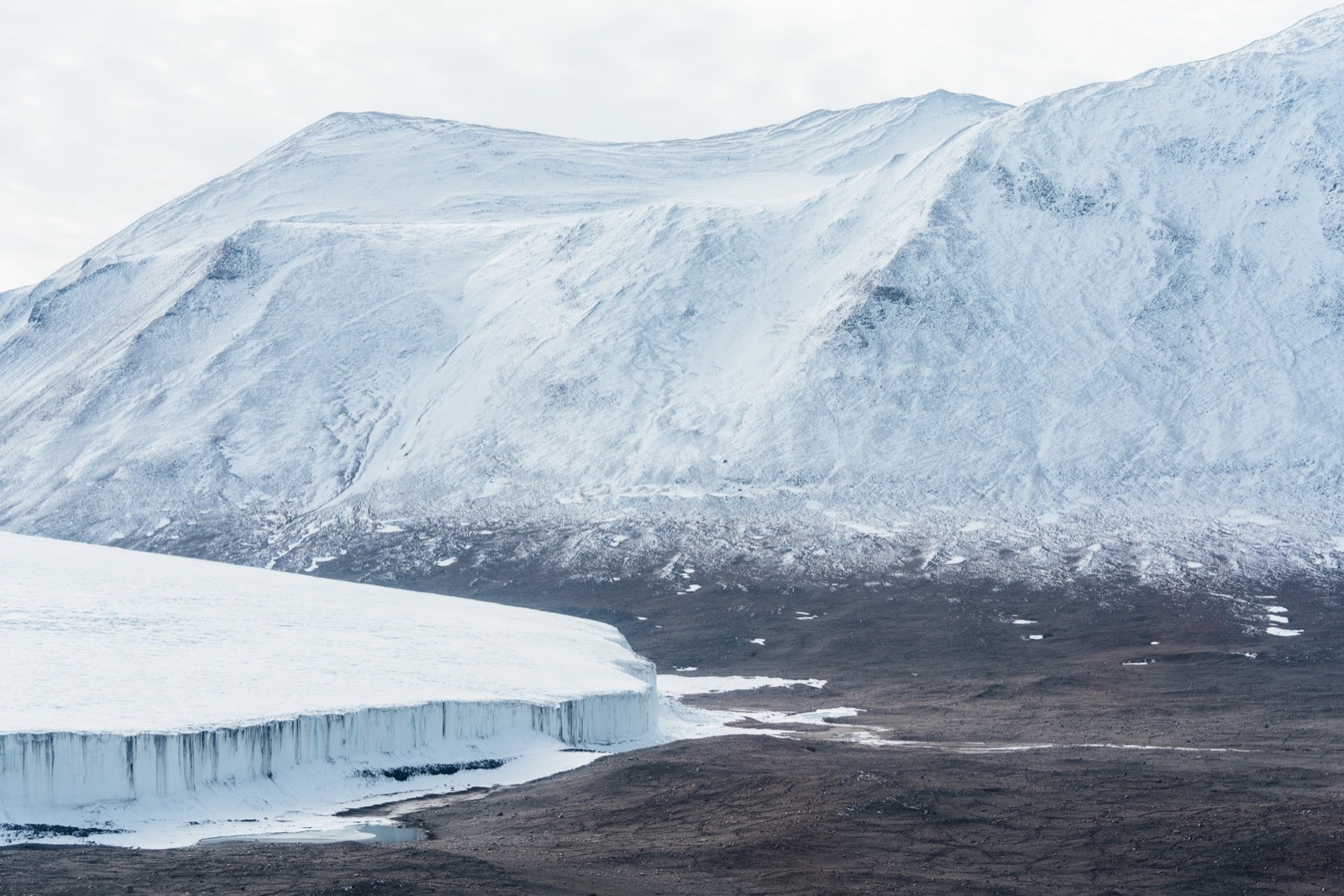  a beautiful landscape shot of white, baby blue capped mountains. below at the base of the mountain is a large glacier 