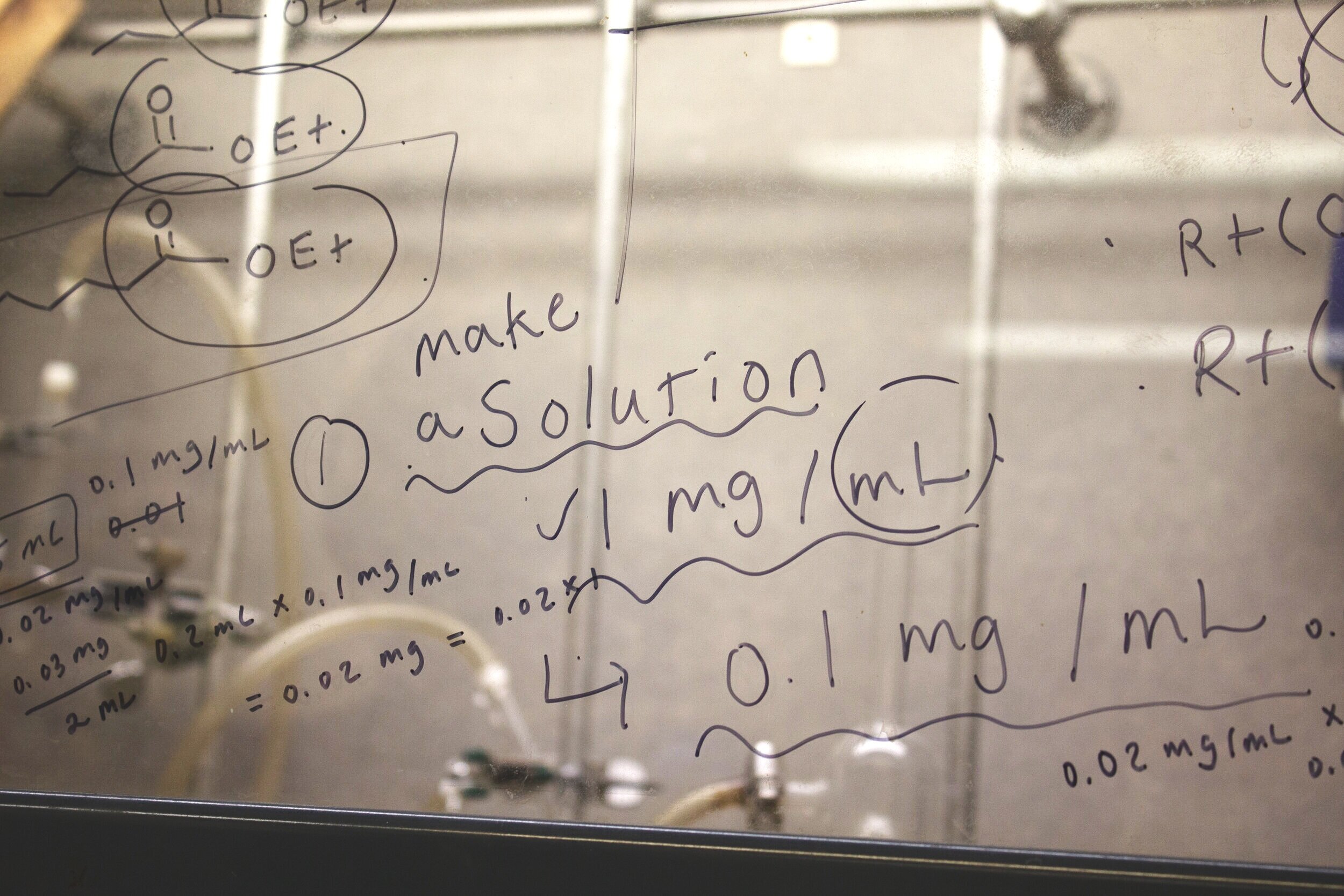  A glass partition is covered with chemical formulas, equations, and measurements in dry erase marker.  