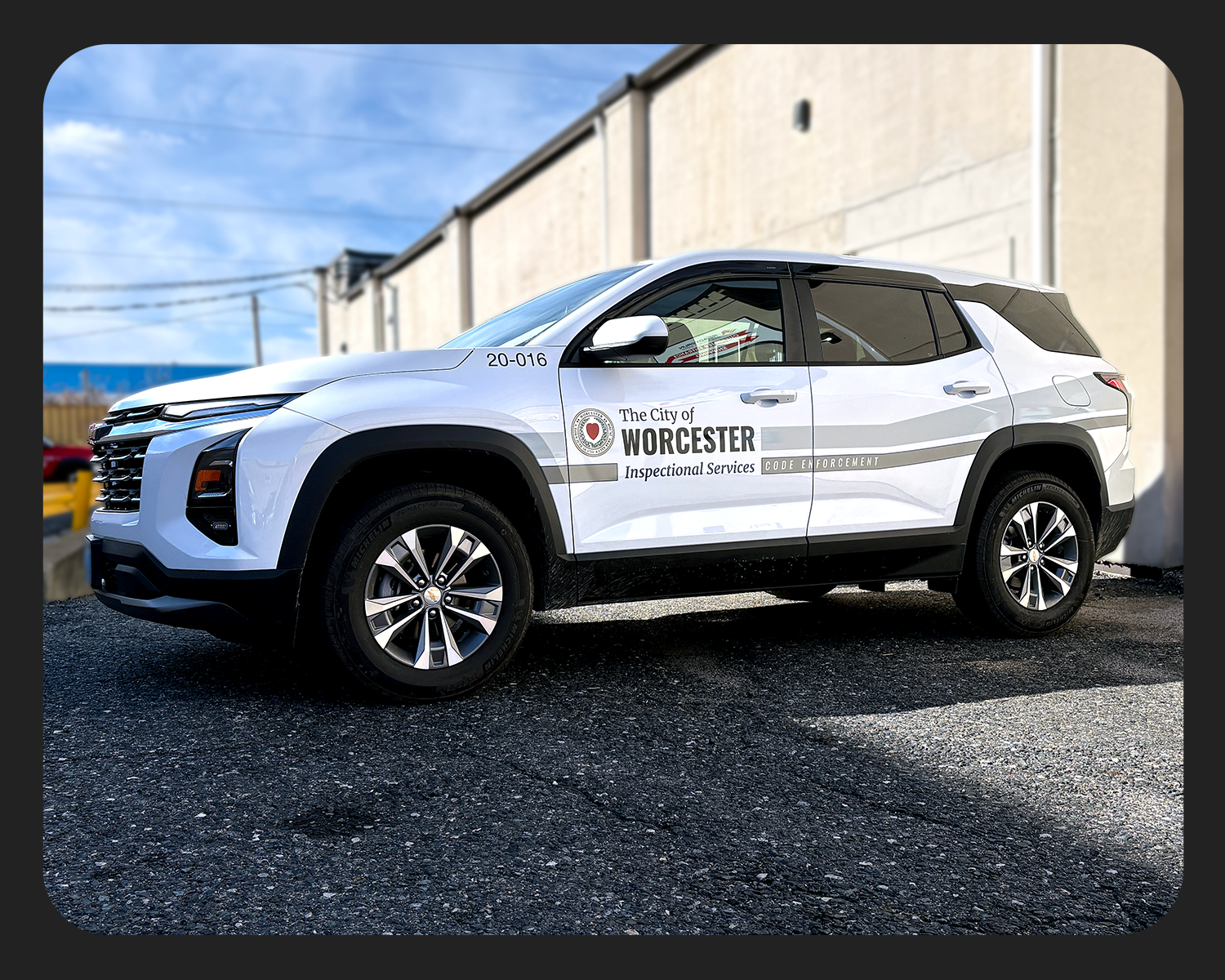 A white police SUV from the City of Worcester Inspectional Services parked on a pavement, with a beige building and a partly cloudy blue sky in the background.