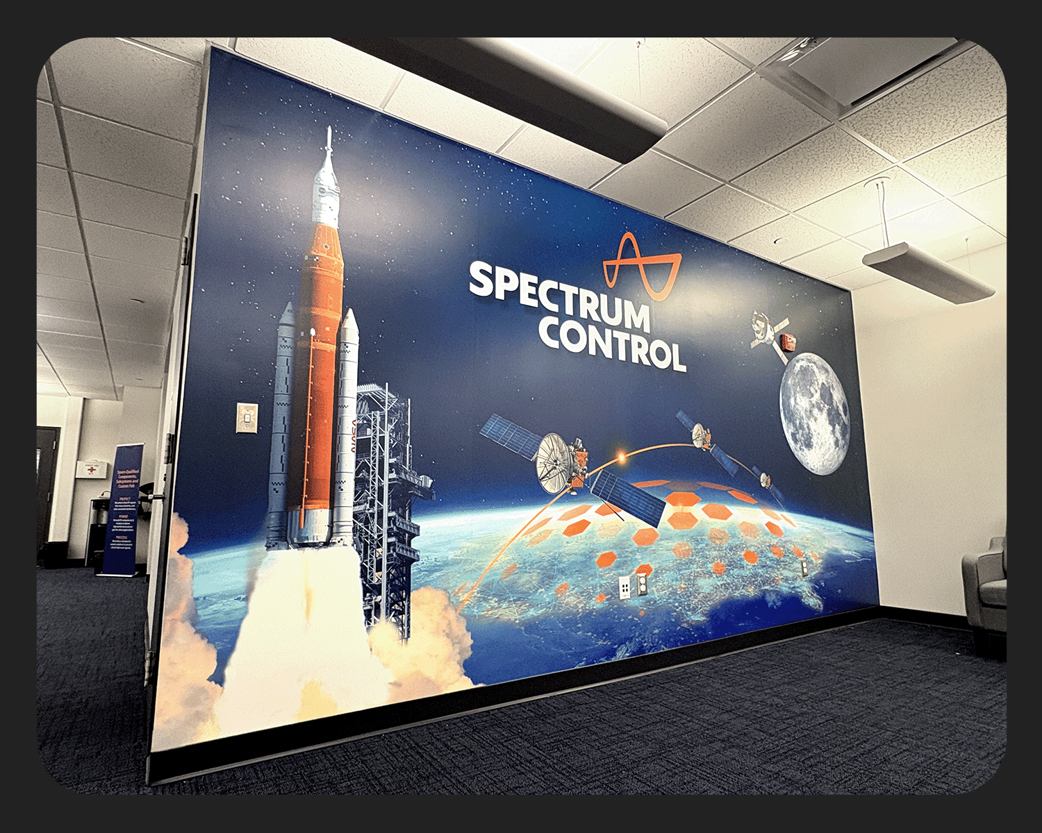 A space-themed mural with a rocket launch, satellites, the moon, and Earth, with the text "Spectrum Control" and a logo at the top.