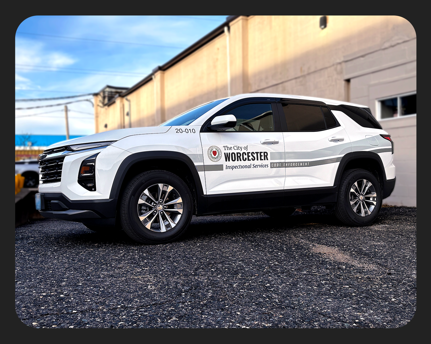 A white SUV with markings indicating it is a Worcester city inspection vehicle parked on a gravel surface in front of a beige building with a window, under a cloudy sky.
