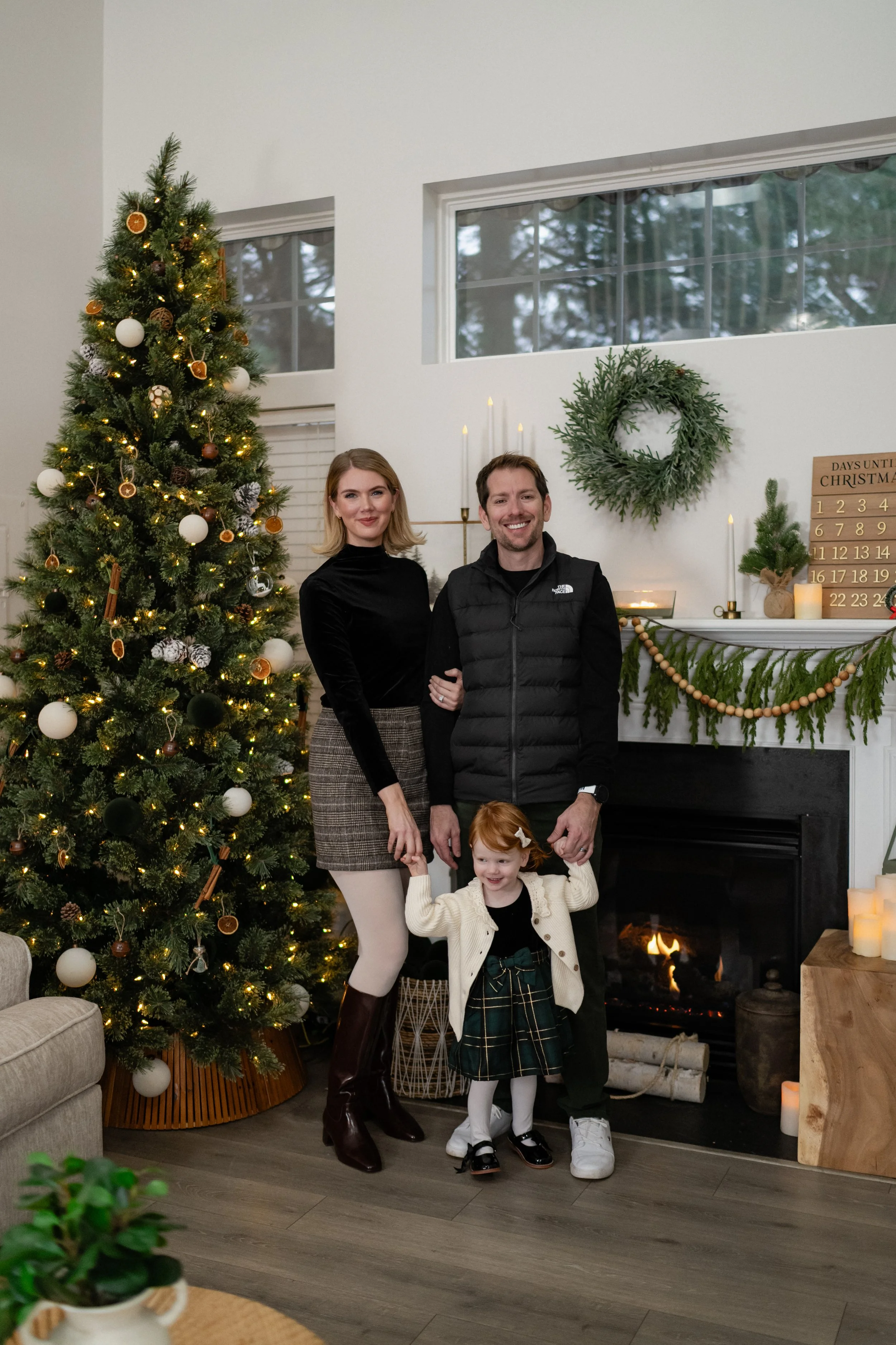 A family posing in front of a Christmas tree and fireplace in a living room, decorated with a wreath and candles, during holiday celebration.
