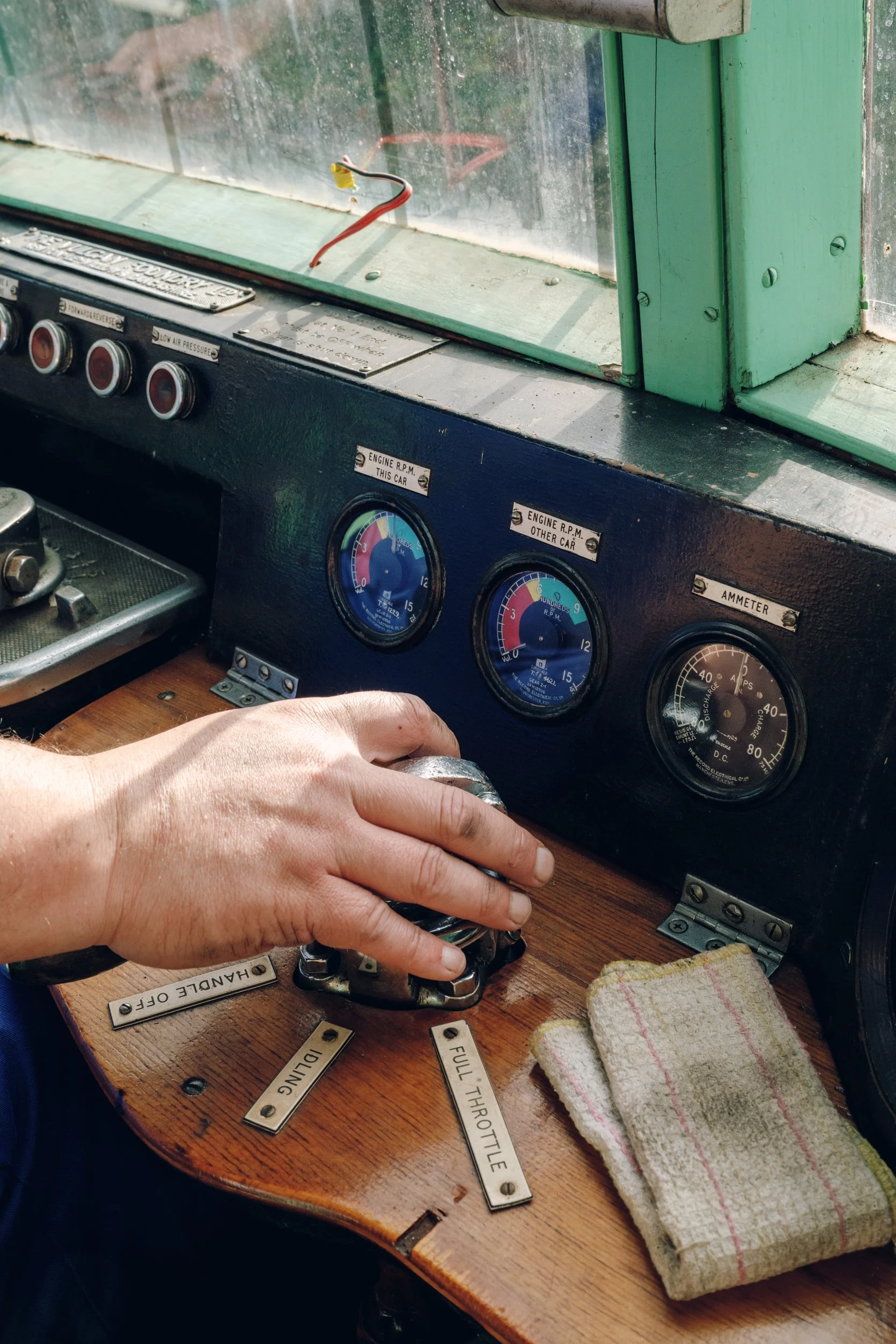 A person's hand is turning a vintage train control lever inside the driver's cabin, with gauges and labels like 'Full Throttle' and 'Danger Off' visible on the wooden dashboard.