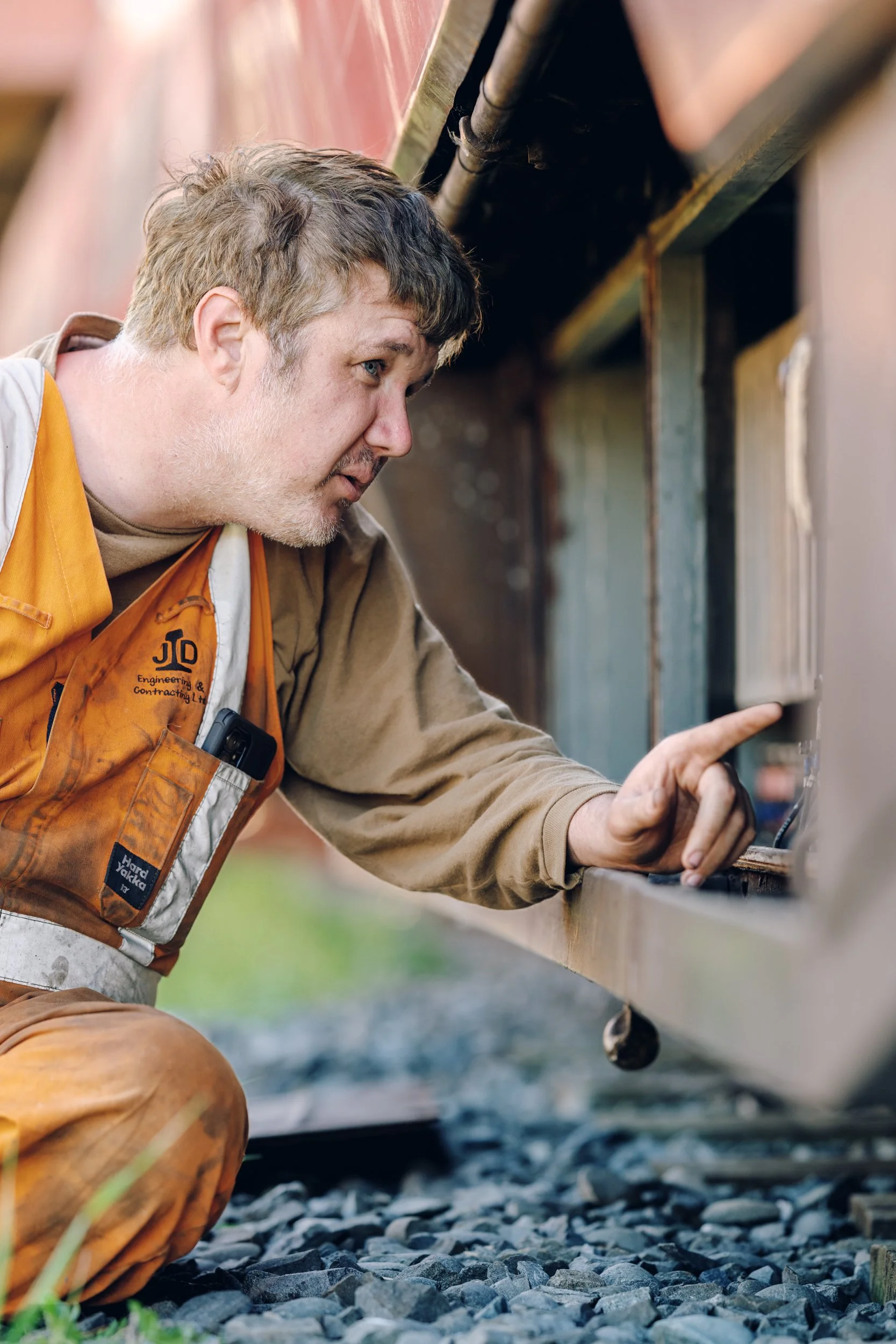 A man inspecting a train wheel while kneeling on the ground outside.