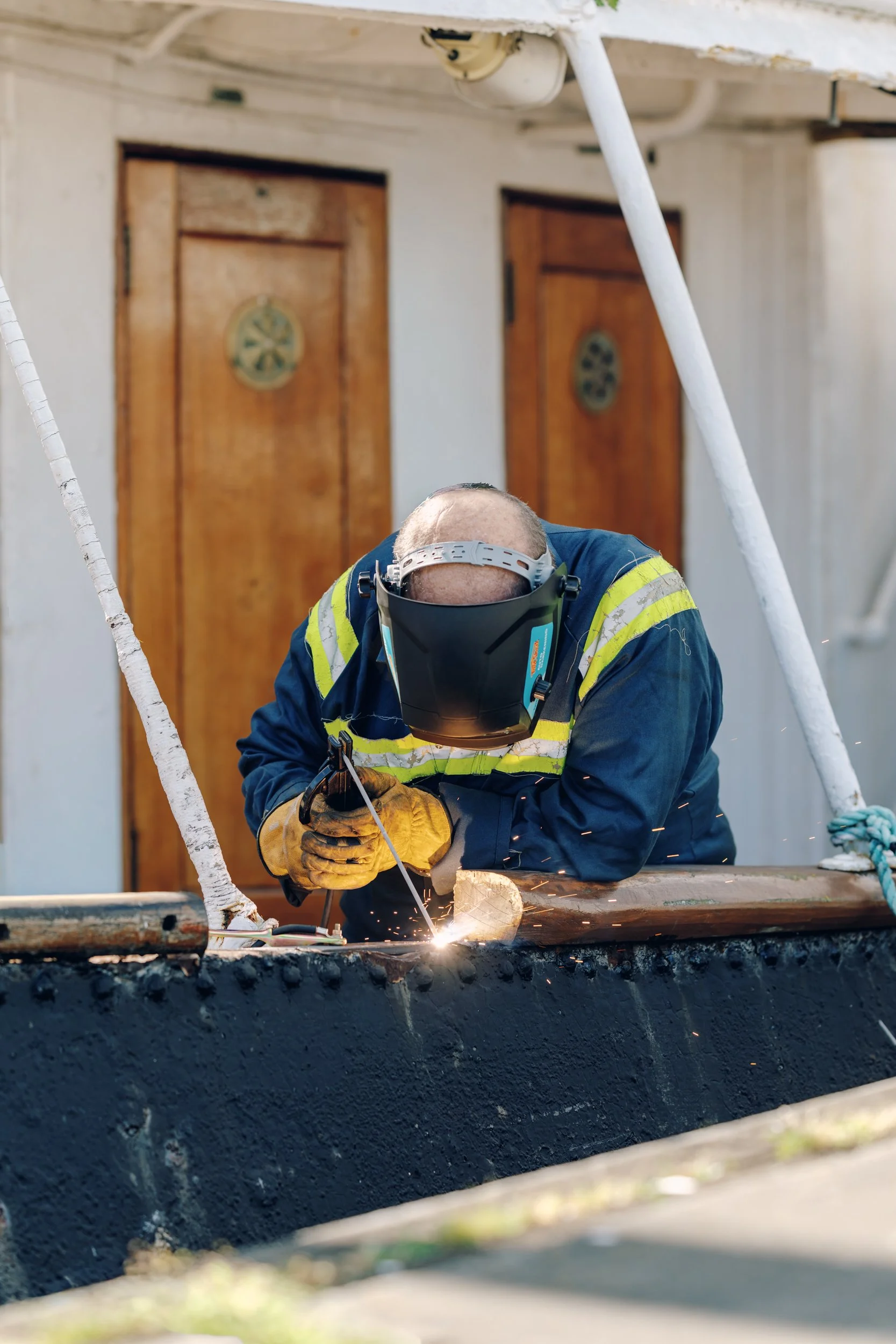 A worker welding on a construction site, wearing safety protective gear including a helmet and gloves, with sparks flying from the welding activity.