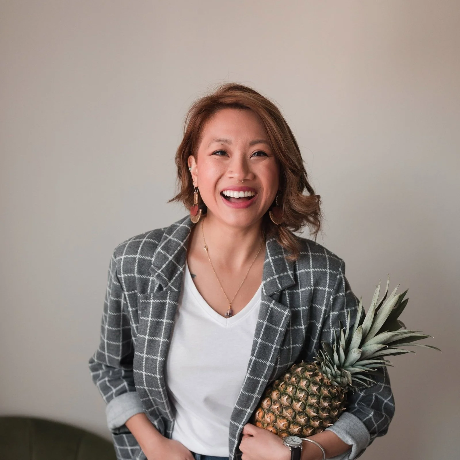 You Belong Here Blog Contributor Cassandra, a light-skinned Asian person with light brown hair smiles at the camera holding a pineapple.