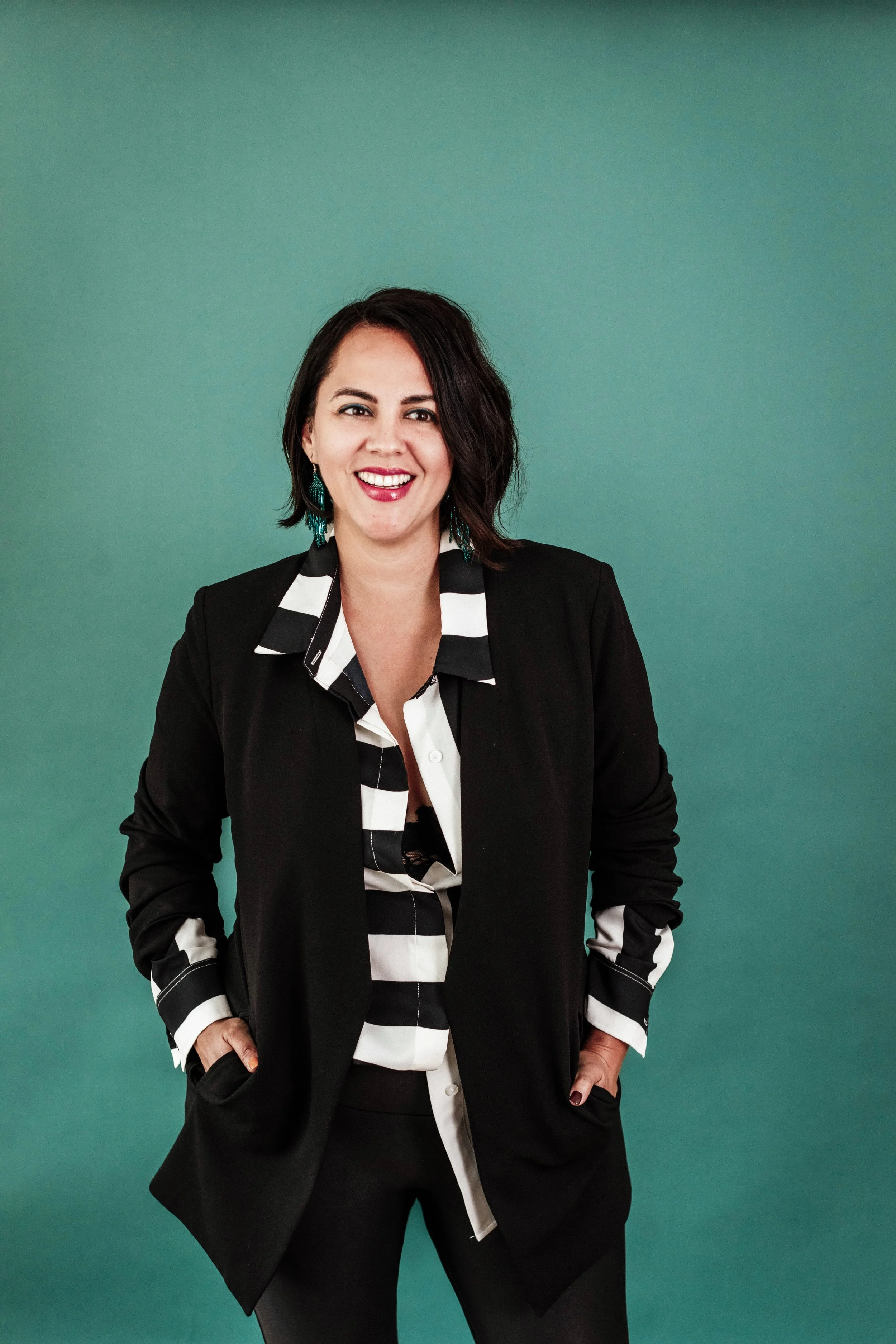You Belong Here CEO and Program Director Nic Roc, a light skinned Latinx woman with dark hair, stands in front of a blue background.