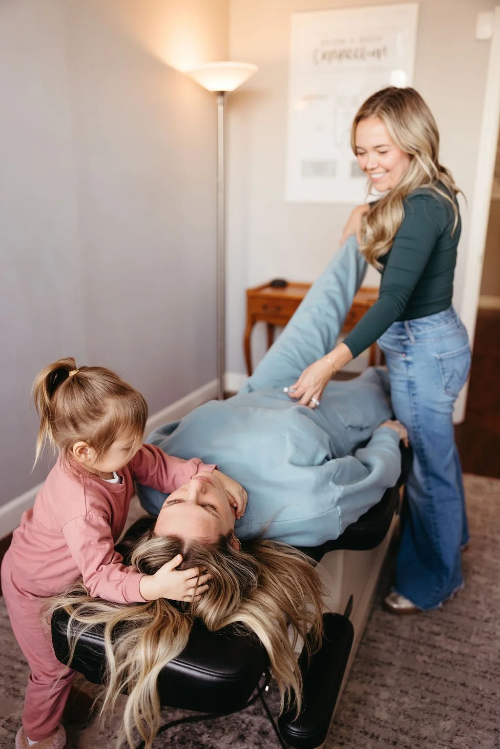 Women adjusting a mom with a child at her chiropractic office using applied kinesiology.