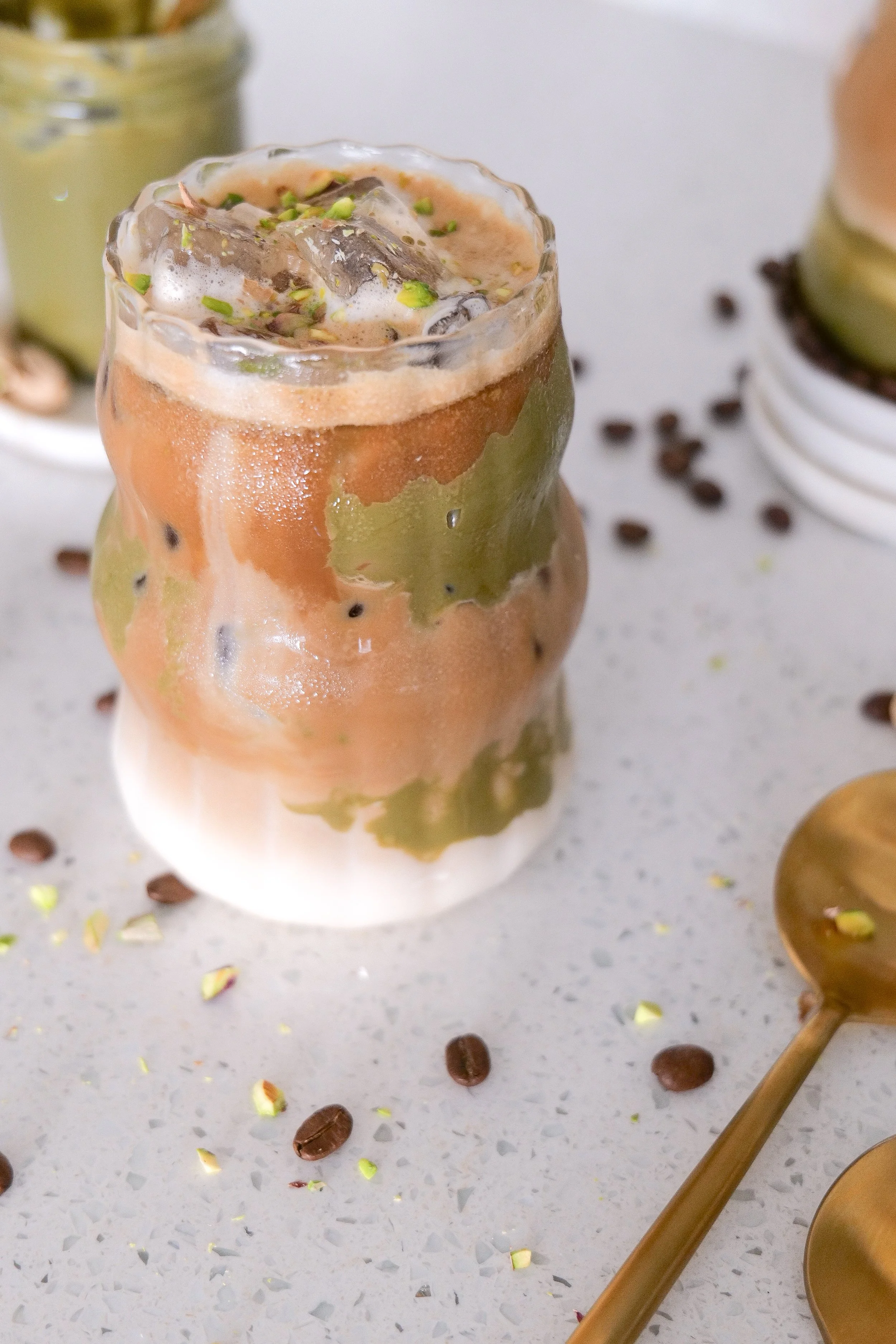 Creamy iced pistachio latte served in a clear glass with espresso and milk layered over ice.