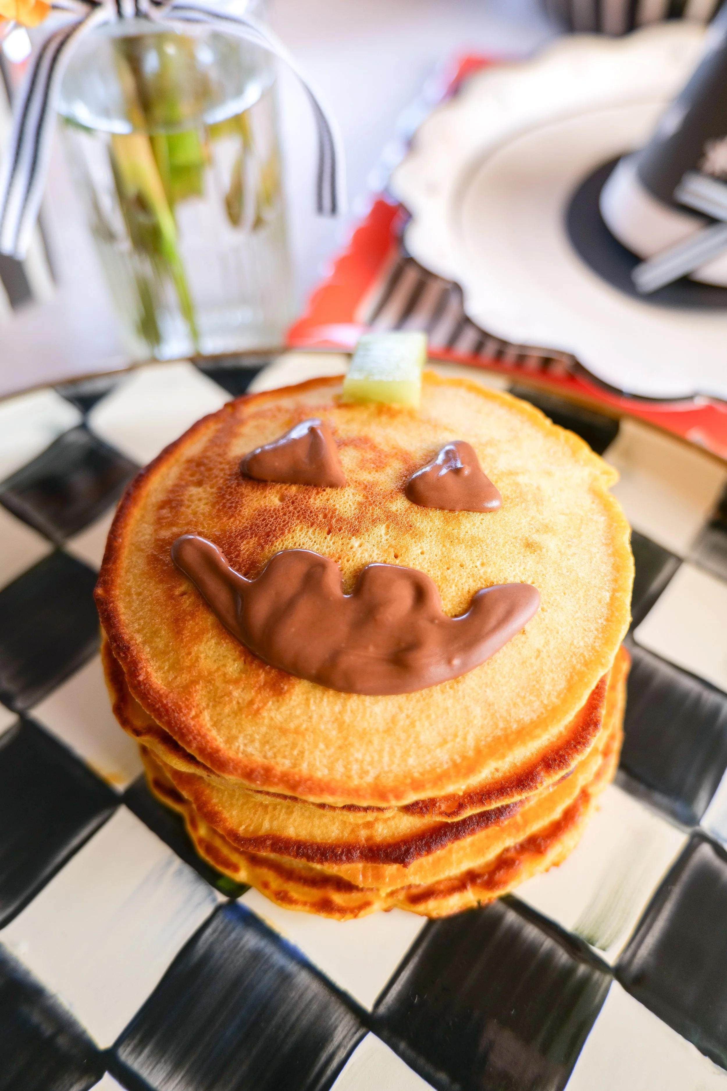 Pumpkin Halloween pancake decorated with a kiwi stem and melted chocolate jack-o-lantern face.