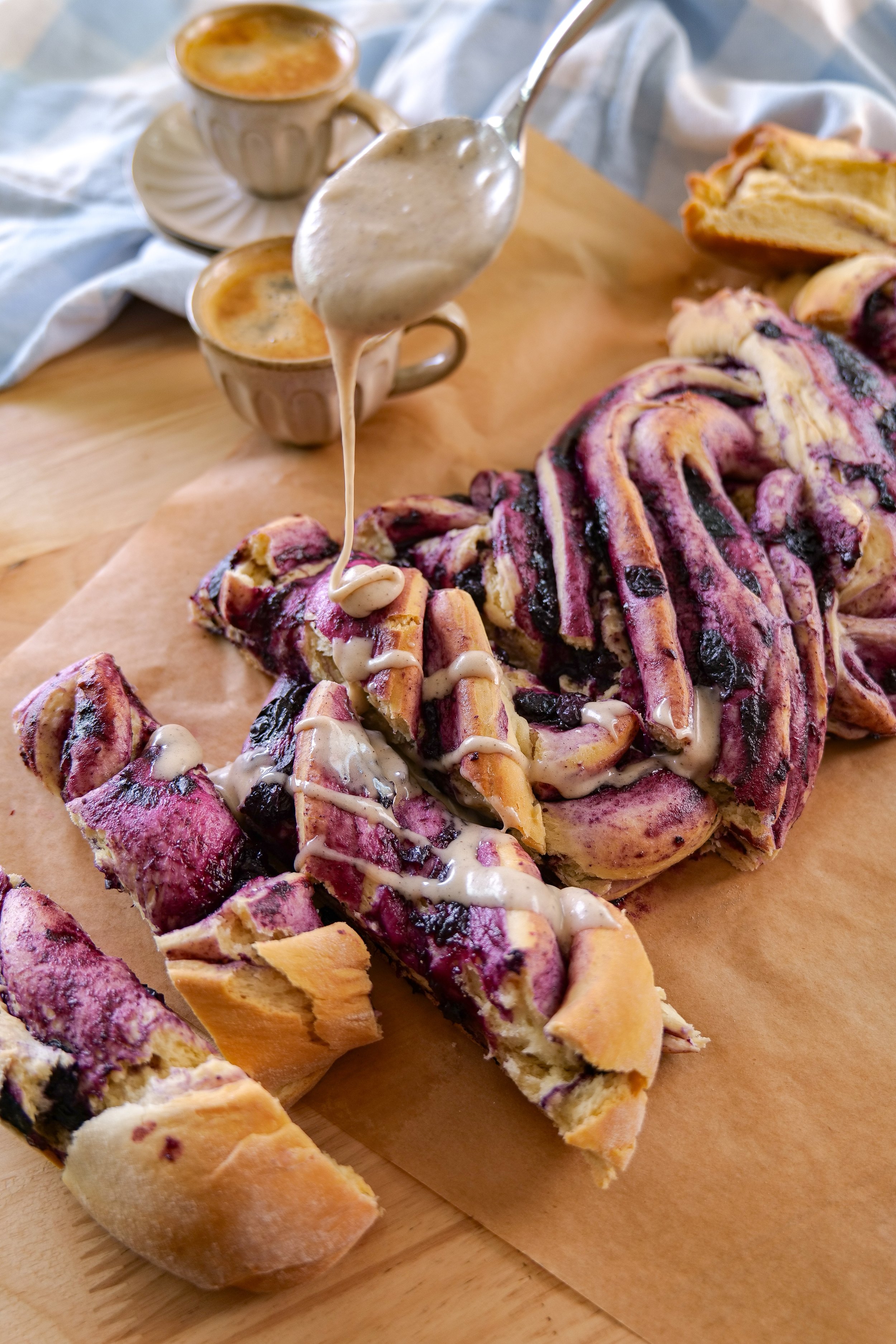 Brown butter vanilla icing drizzled over a warm homemade blueberry cinnamon roll loaf.