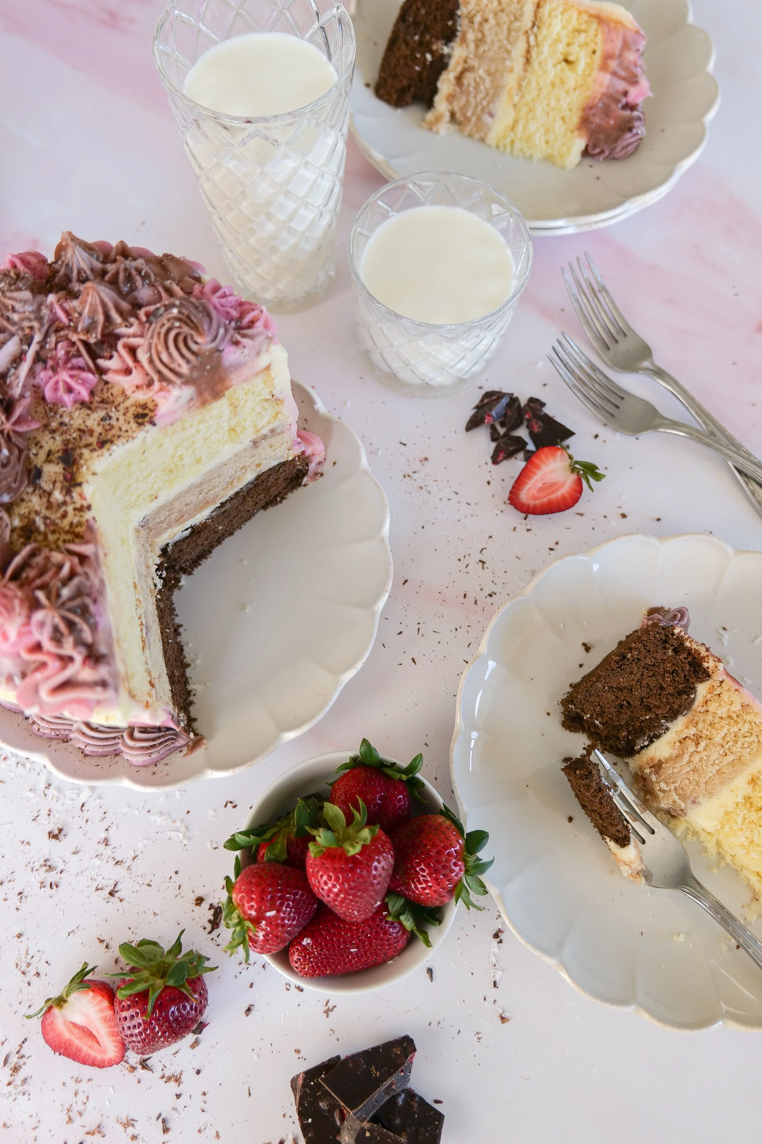 layered Neapolitan cake with strawberries and milk on a table.